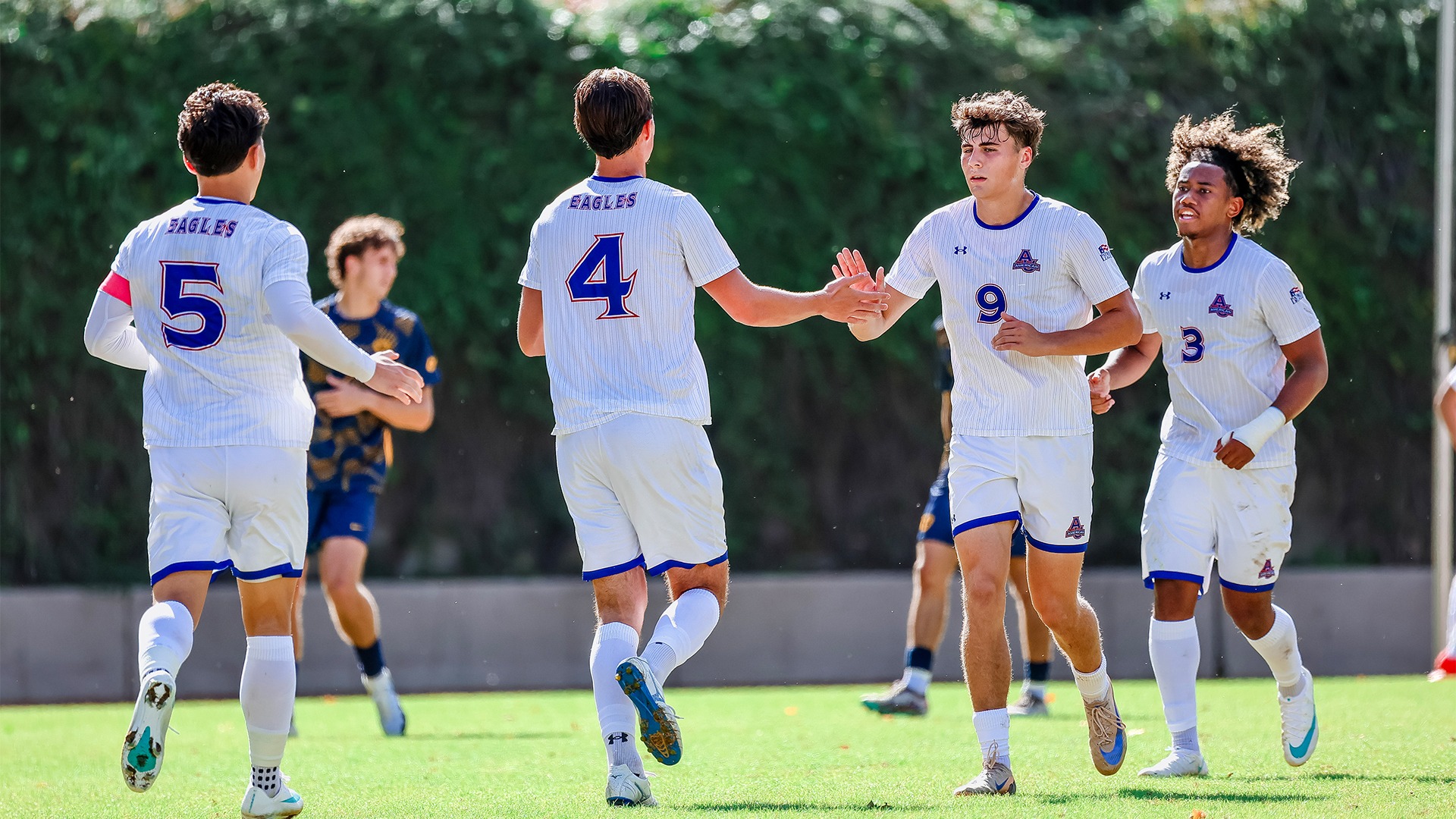 Two men's soccer players subbing off the field and two players coming on. 