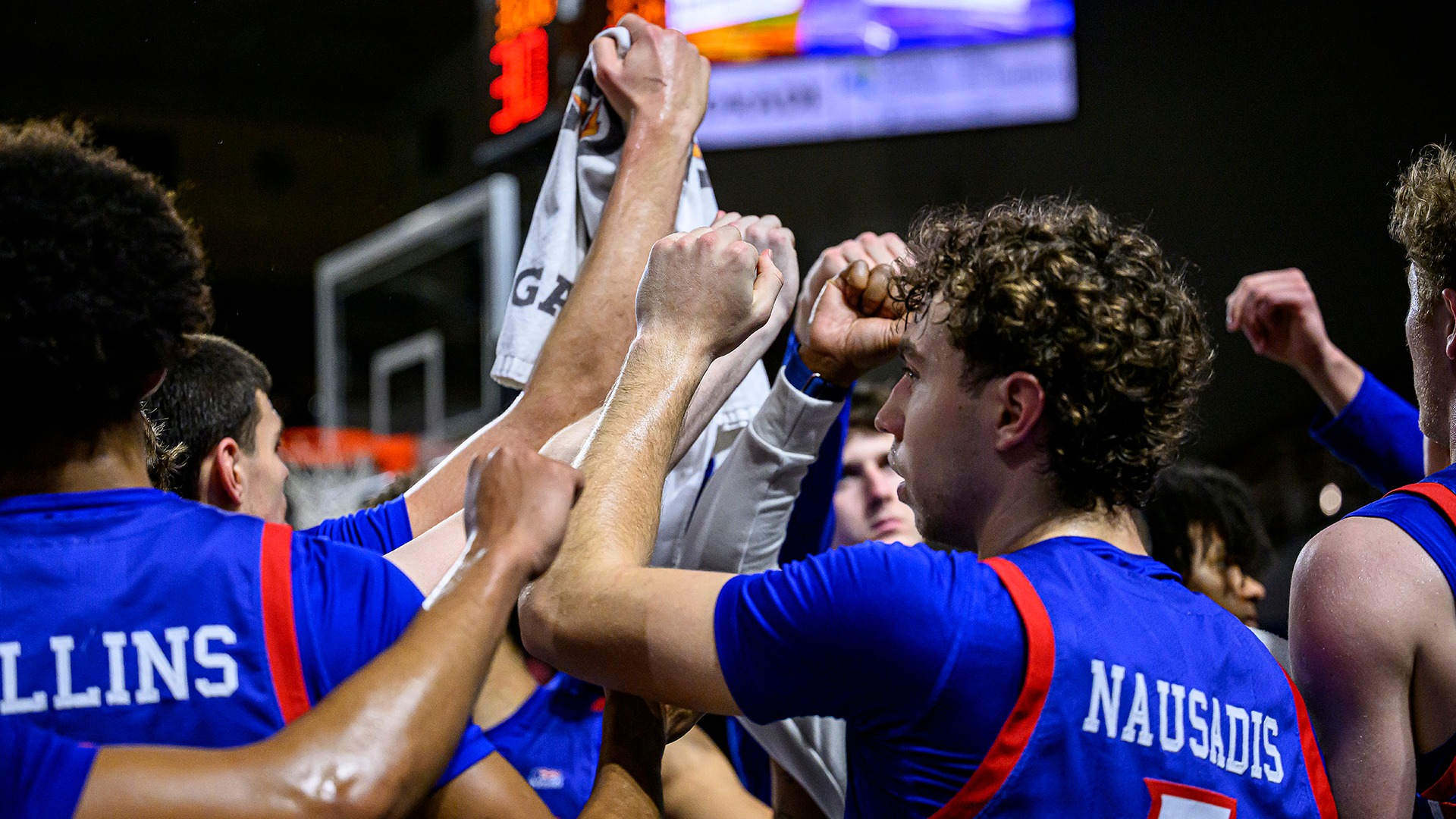 men's basketball players huddled with hands up