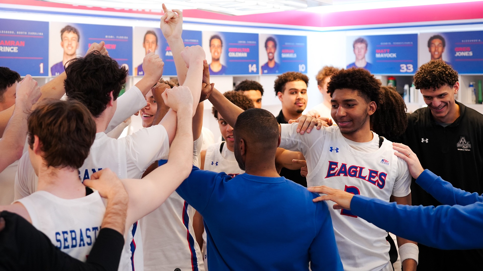 men's basketball team huddled with hands up in their locker room