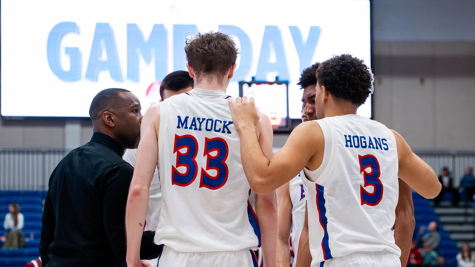 men's basketball players huddled with head coach Duane Simpkins