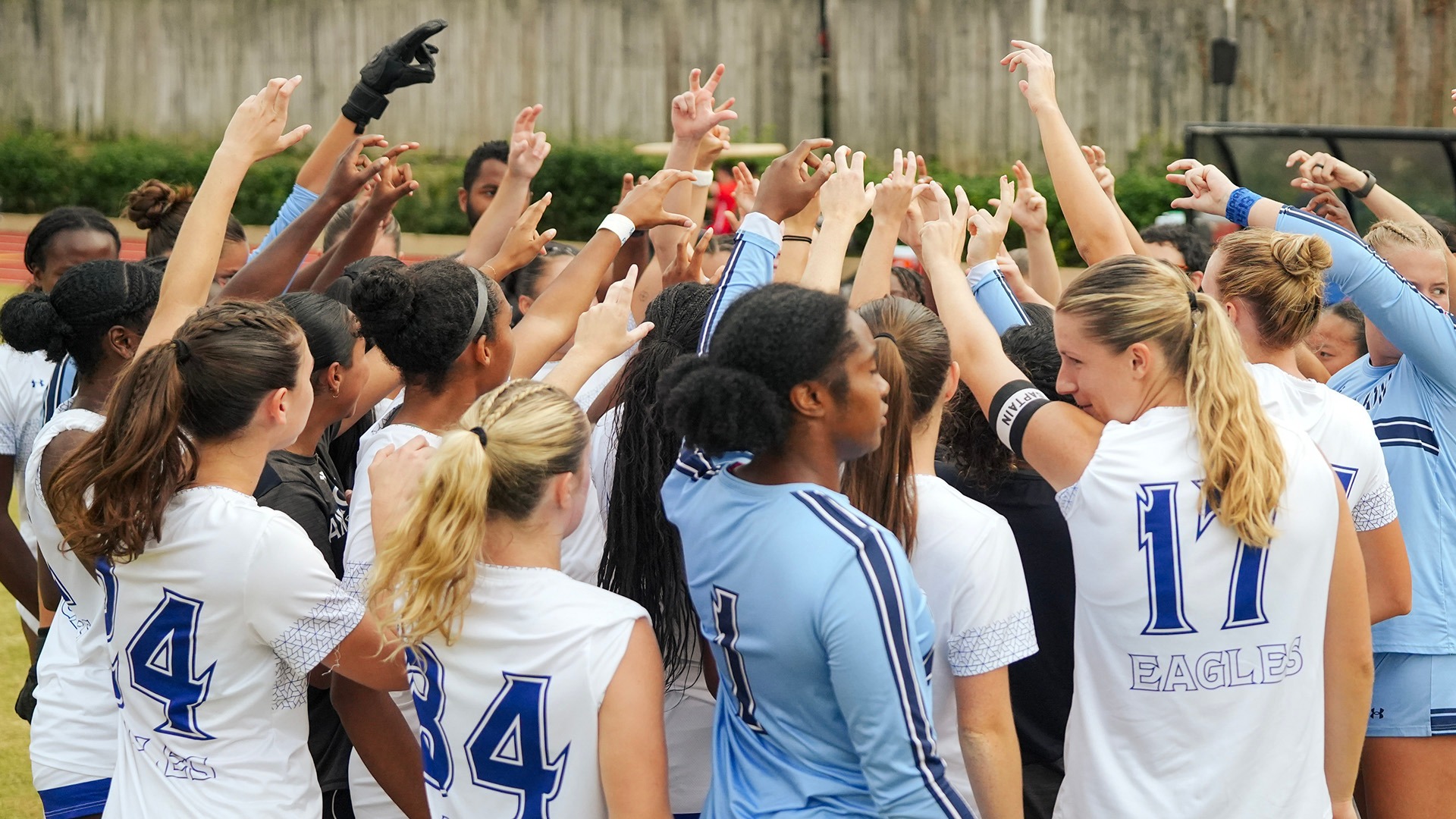 women's soccer players huddled with hands in the air