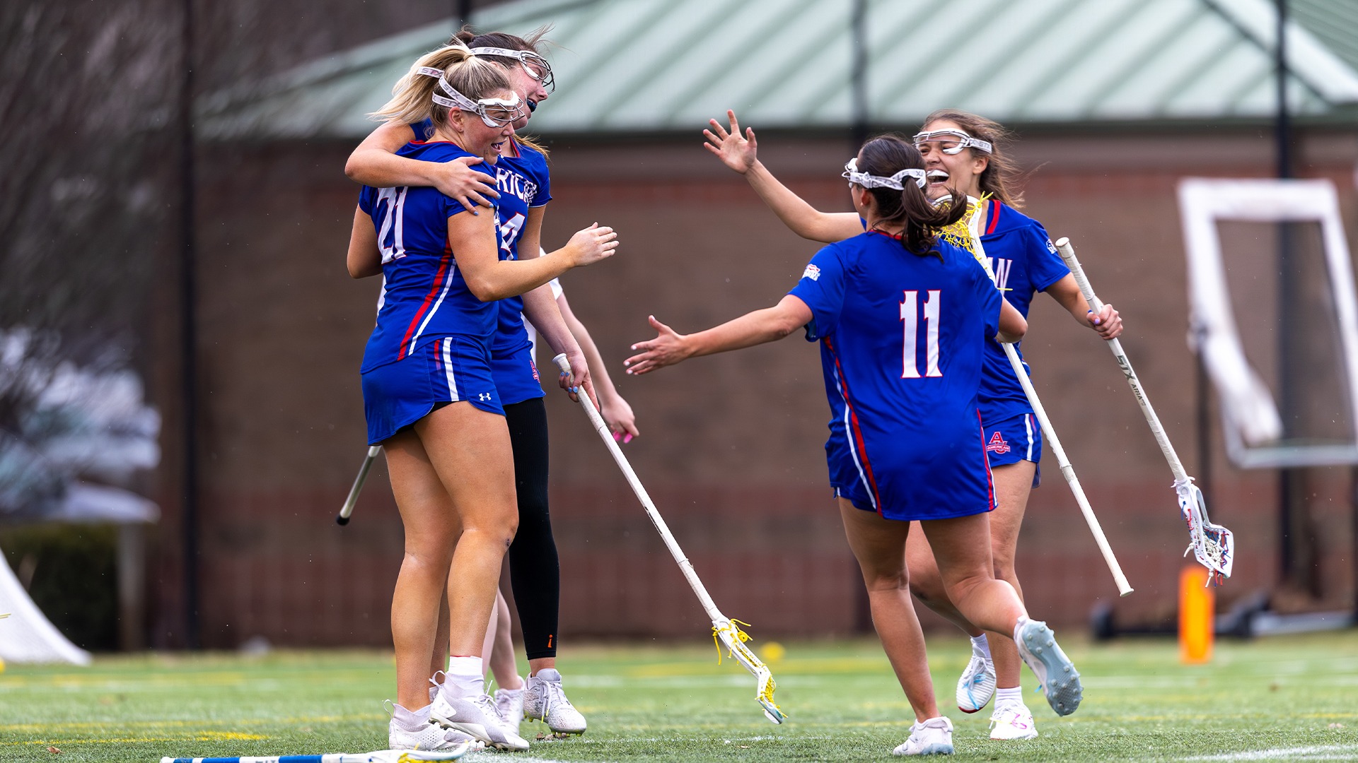 Kellie Linehan, Reagan Murdoch, Julia Pope, and Adria Kotzian celebrating a goal in a lacrosse game. 