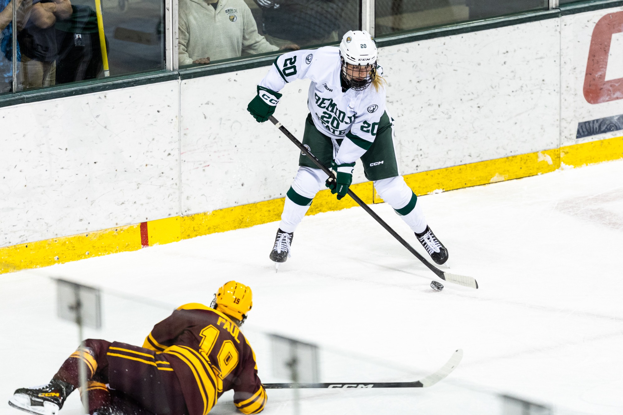 Elly Klepinger controls the puck along the boards while a Minnesota player falls to the ice nearby.