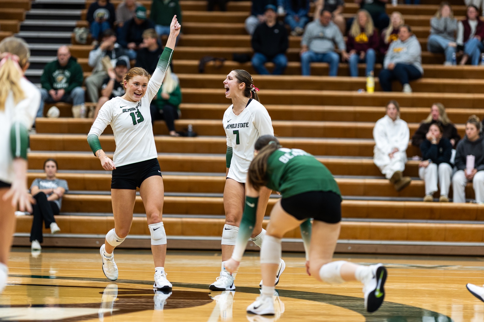Ava Athman and Madi Tripp celebrate a point against UMC, wearing white jerseys with green letters and numbers. 