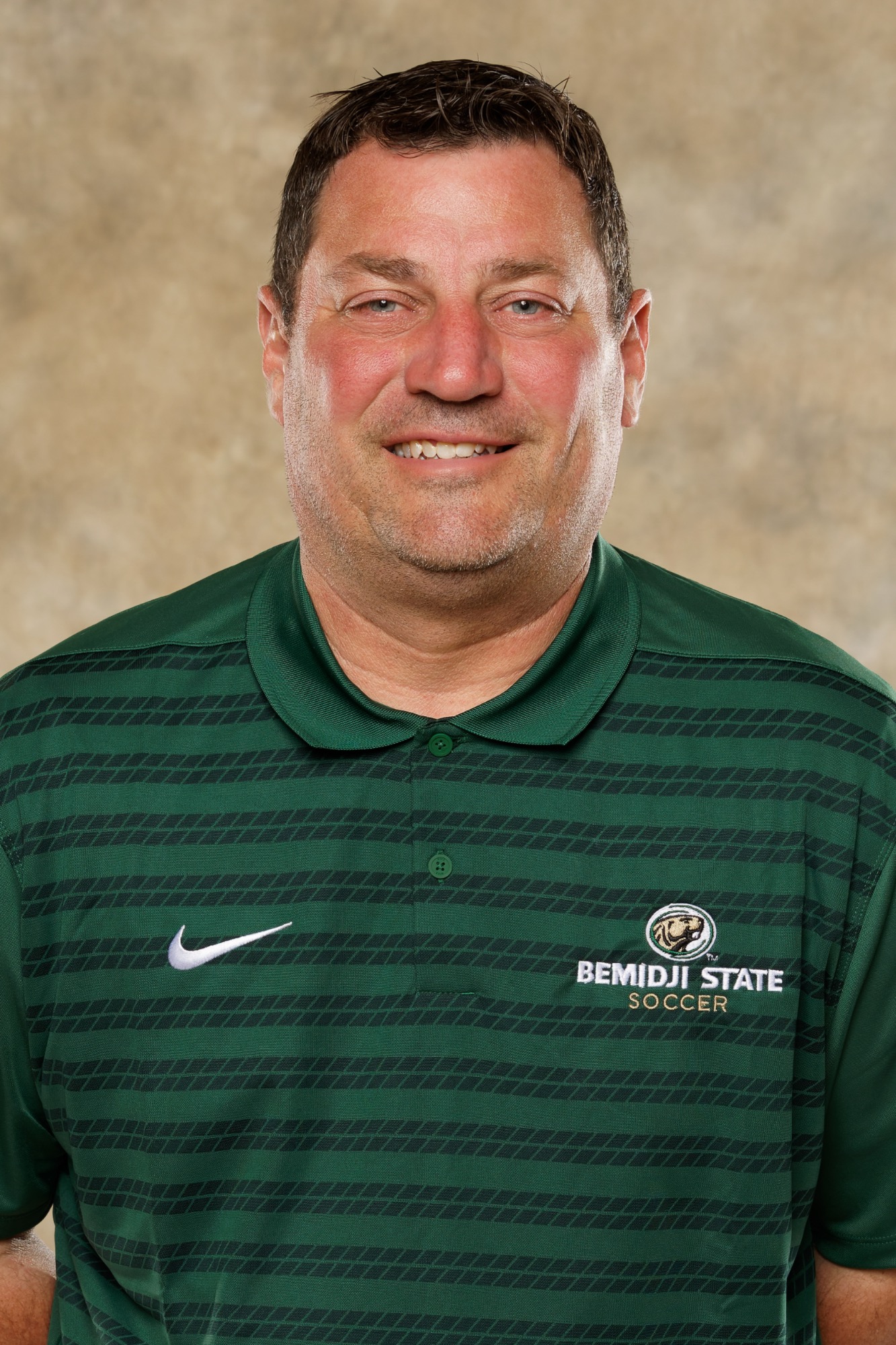 Portrait of Bemidji State soccer coach in green Bemidji State Soccer polo shirt with short dark hair