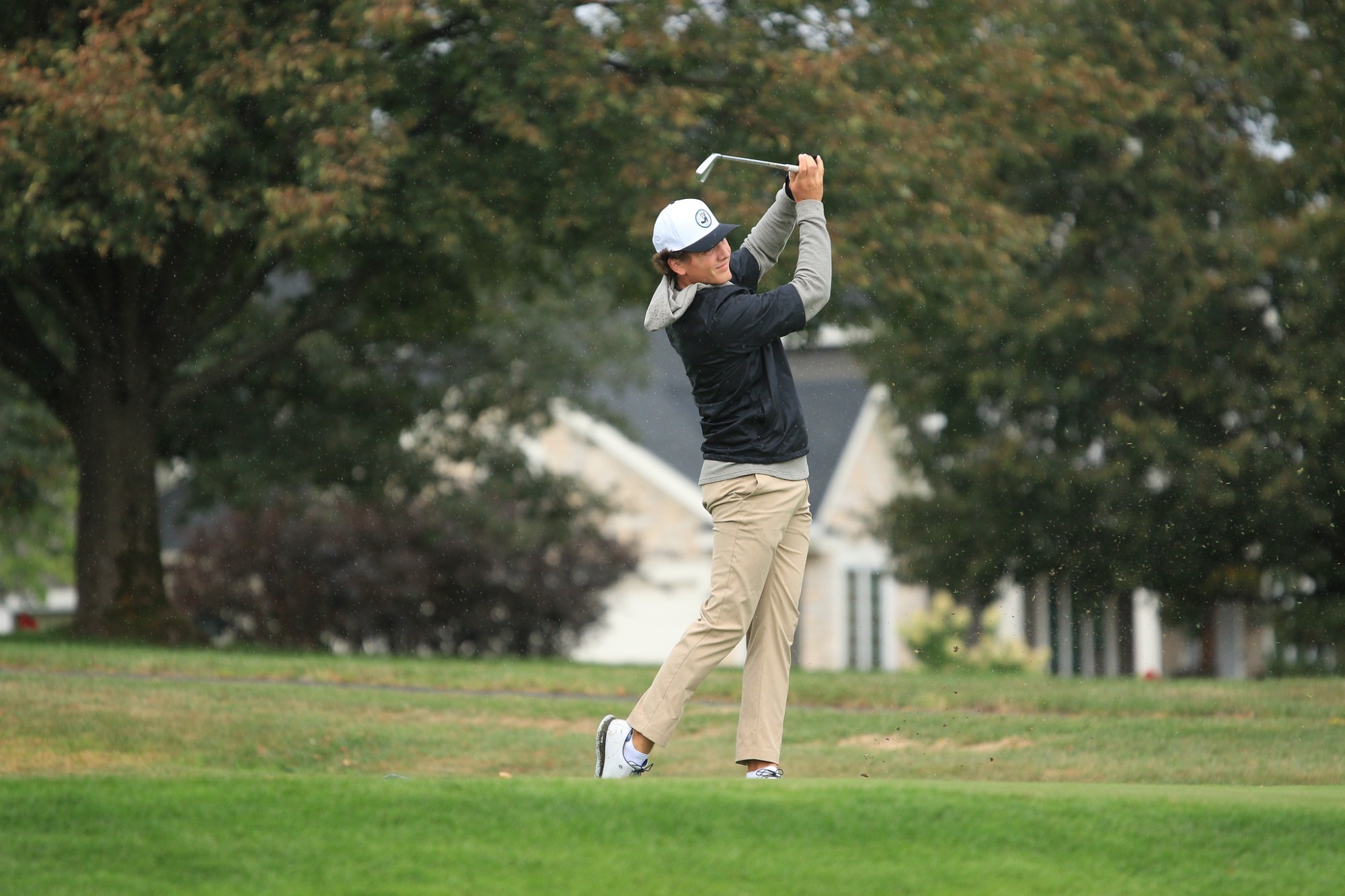 Myles Jorde follows through on a swing during a round, standing on the fairway with trees and a golf course in the background.