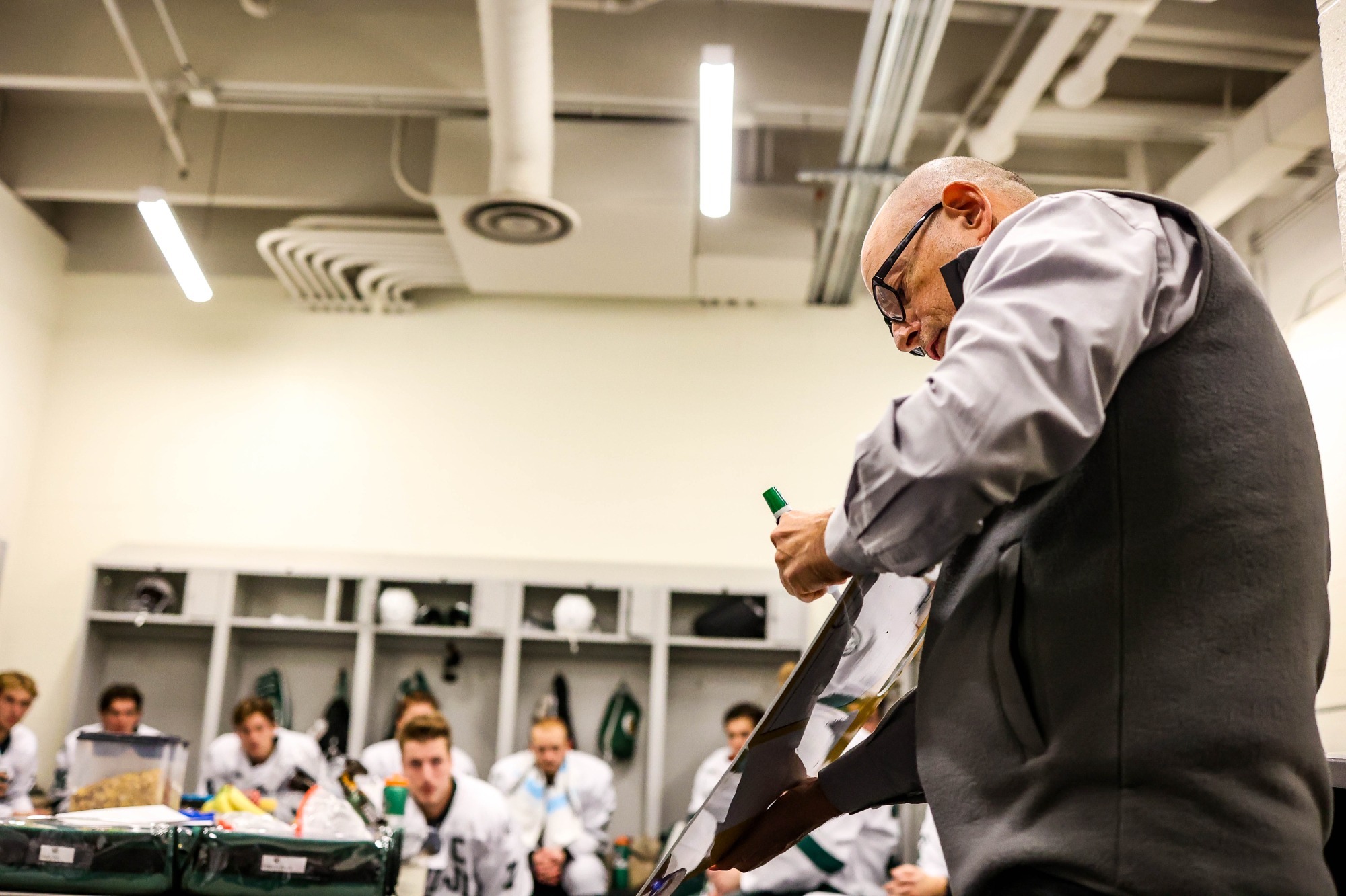 Tom Serratore writes on a whiteboard while speaking to players gathered in the locker room between periods.