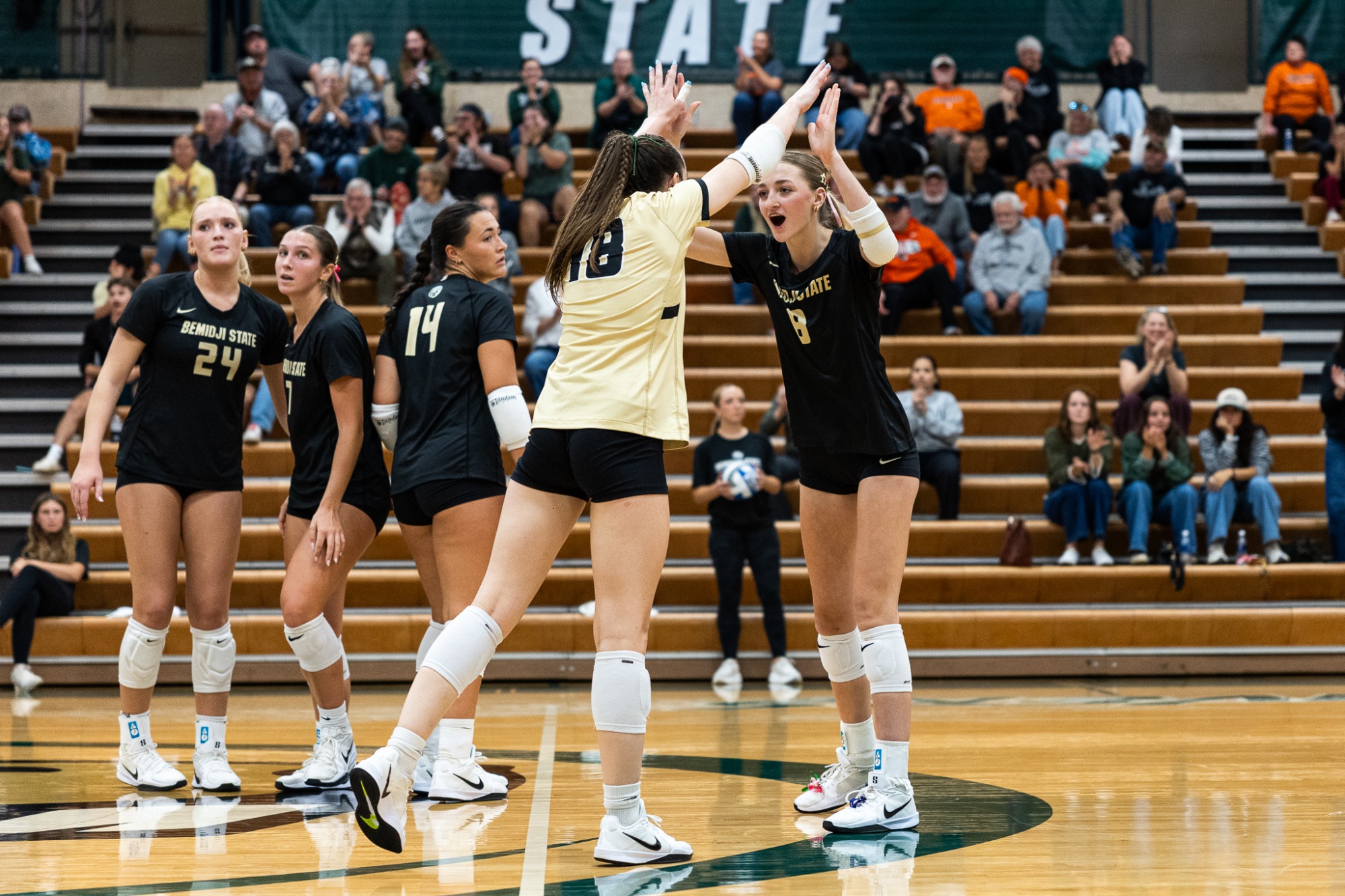 Bemidji State libero No. 18 and teammate No. 8 exchange a high-five while teammates regroup after a point.