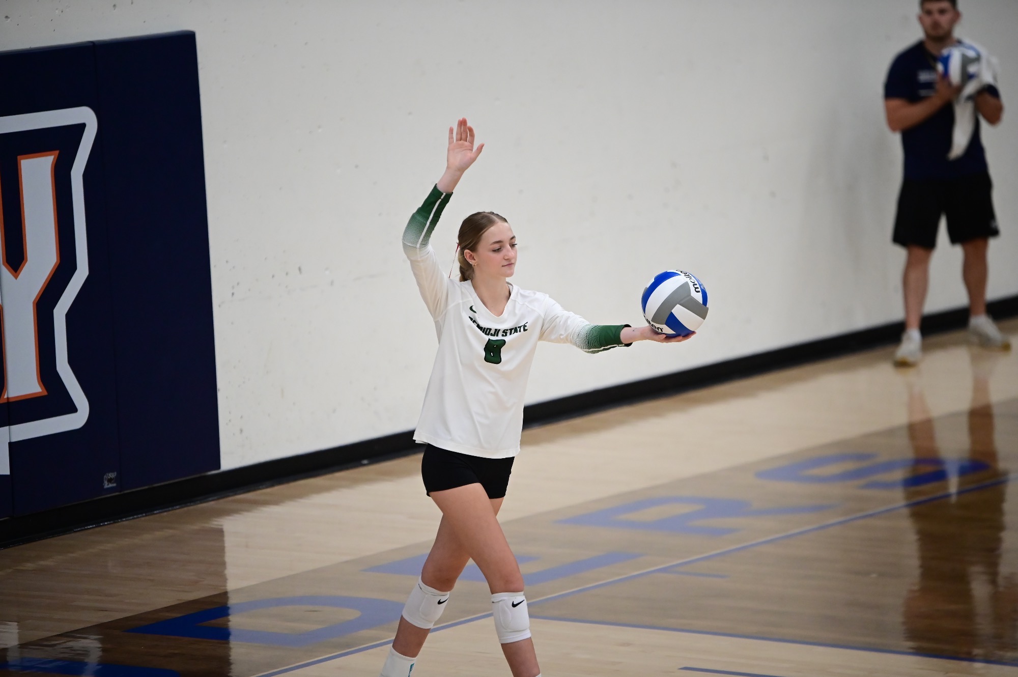 Kayla Gallagher steps to serve in a white, long-sleeve BSU Volleyball jersey with green numbers.