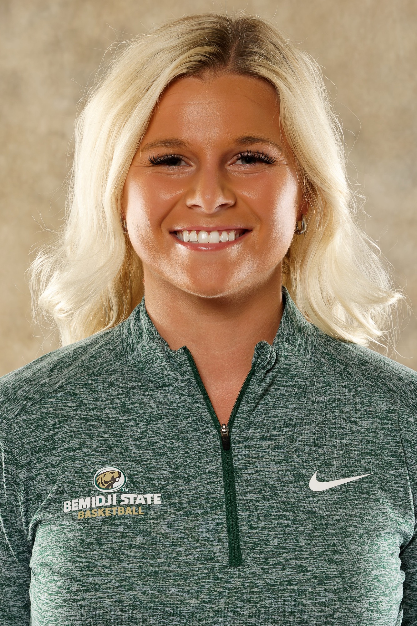 Head Coach Madison McKeever poses for an official Bemidji State women's basketball staff headshot while wearing a green Bemidji State Basketball quarter-zip.