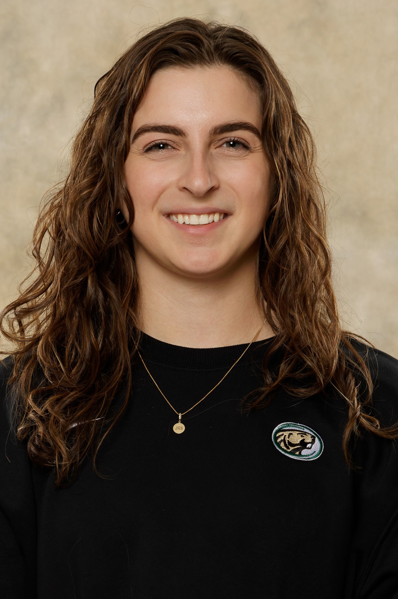 Headshot of Jess Strack wearing a black long sleeve sweater and necklace, facing the camera against a neutral beige backdrop.
