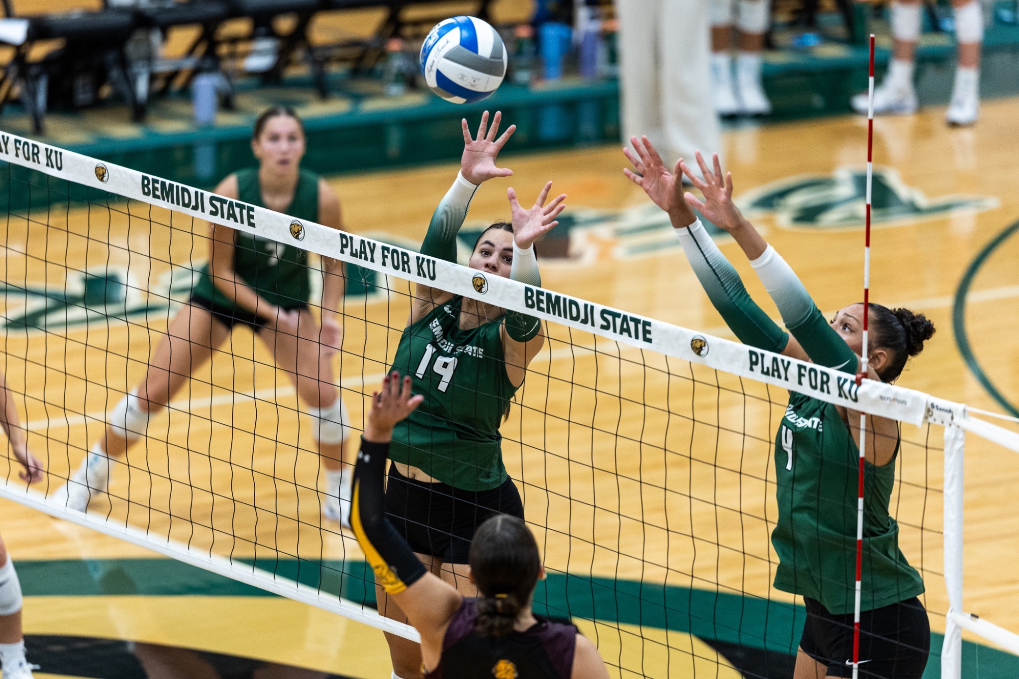BSU's Ella Vander Velden and Nevaeh Carlson reach for a block as a UMD player attacks it at the net. The Beavers are in green jerseys with white 