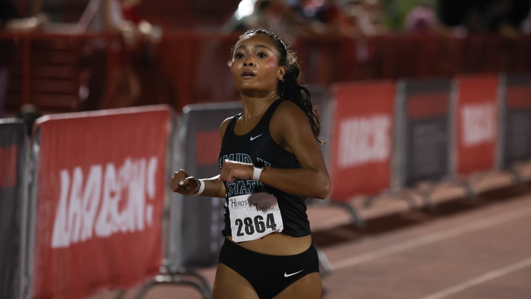 Aleena Vetsouvanh runs across the finish line at the MSUM Dragon twilight. She is wearing a black tank top jersey with green and white decals