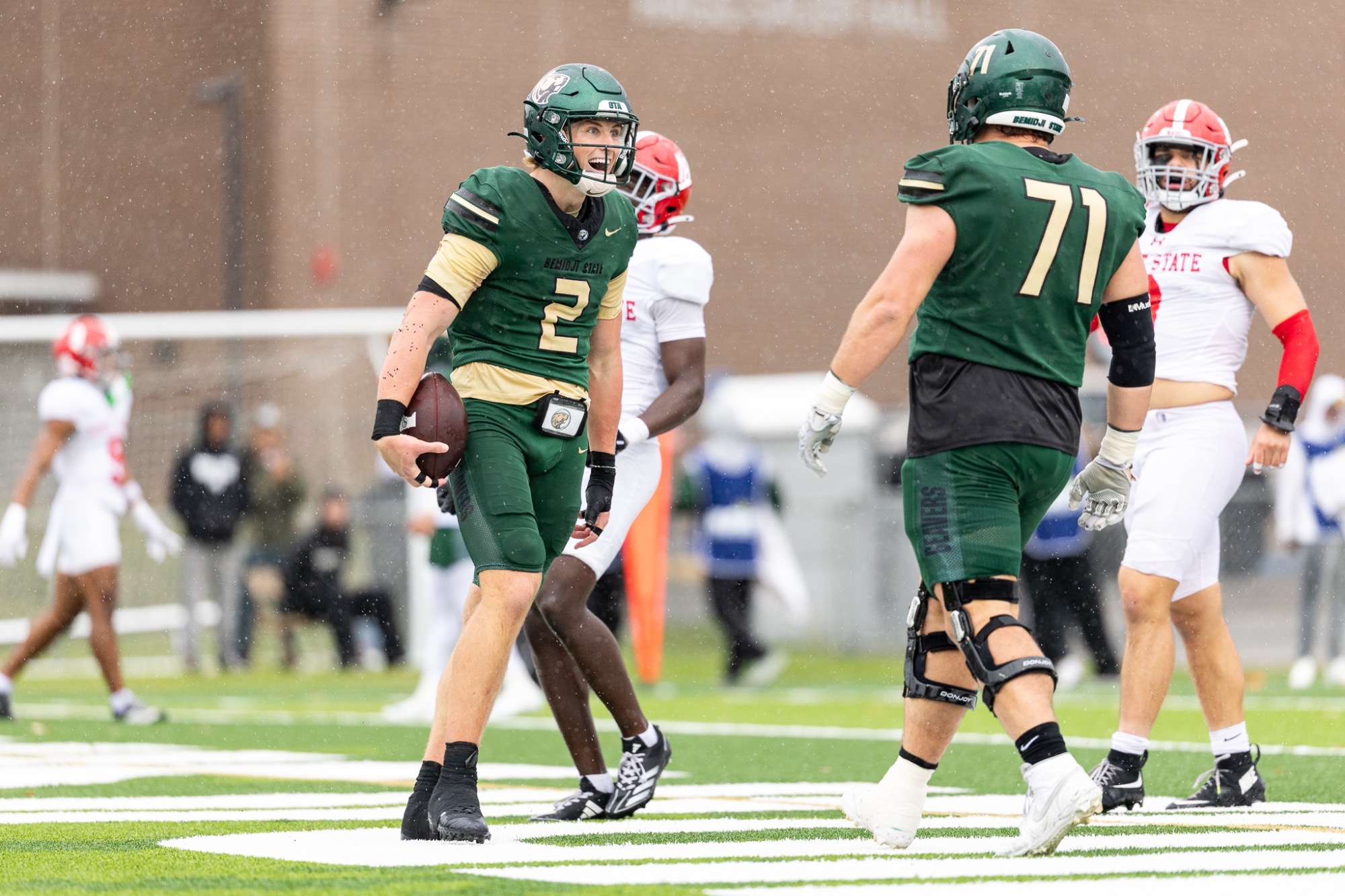 Connor Carver celebrates a touchdown with a teammate during homecoming. The Beavers wear green jerseys and pants with green helmets.