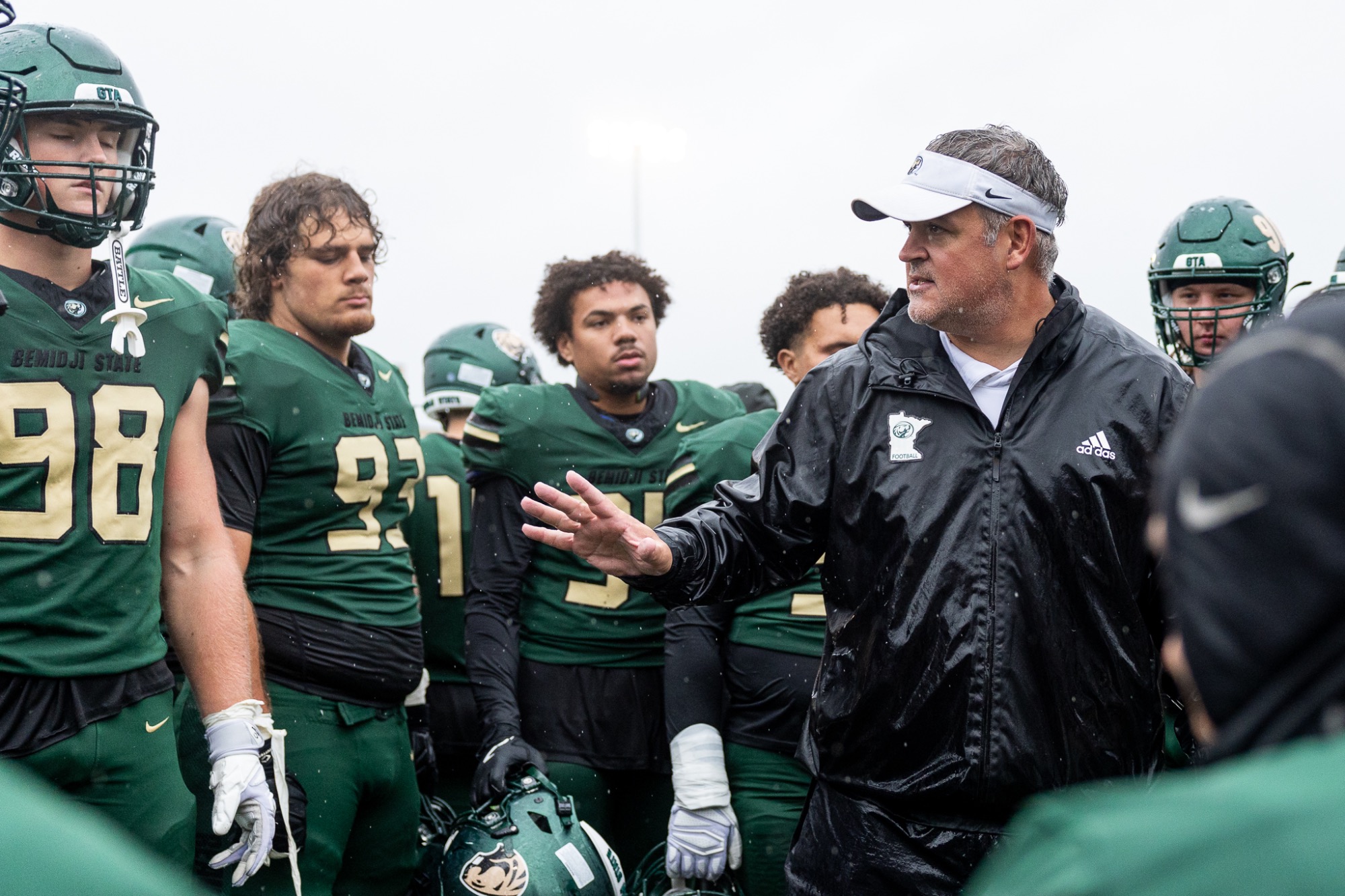 Brent Bolte addresses members of the Bemidji State football team during a sideline huddle in rainy conditions.