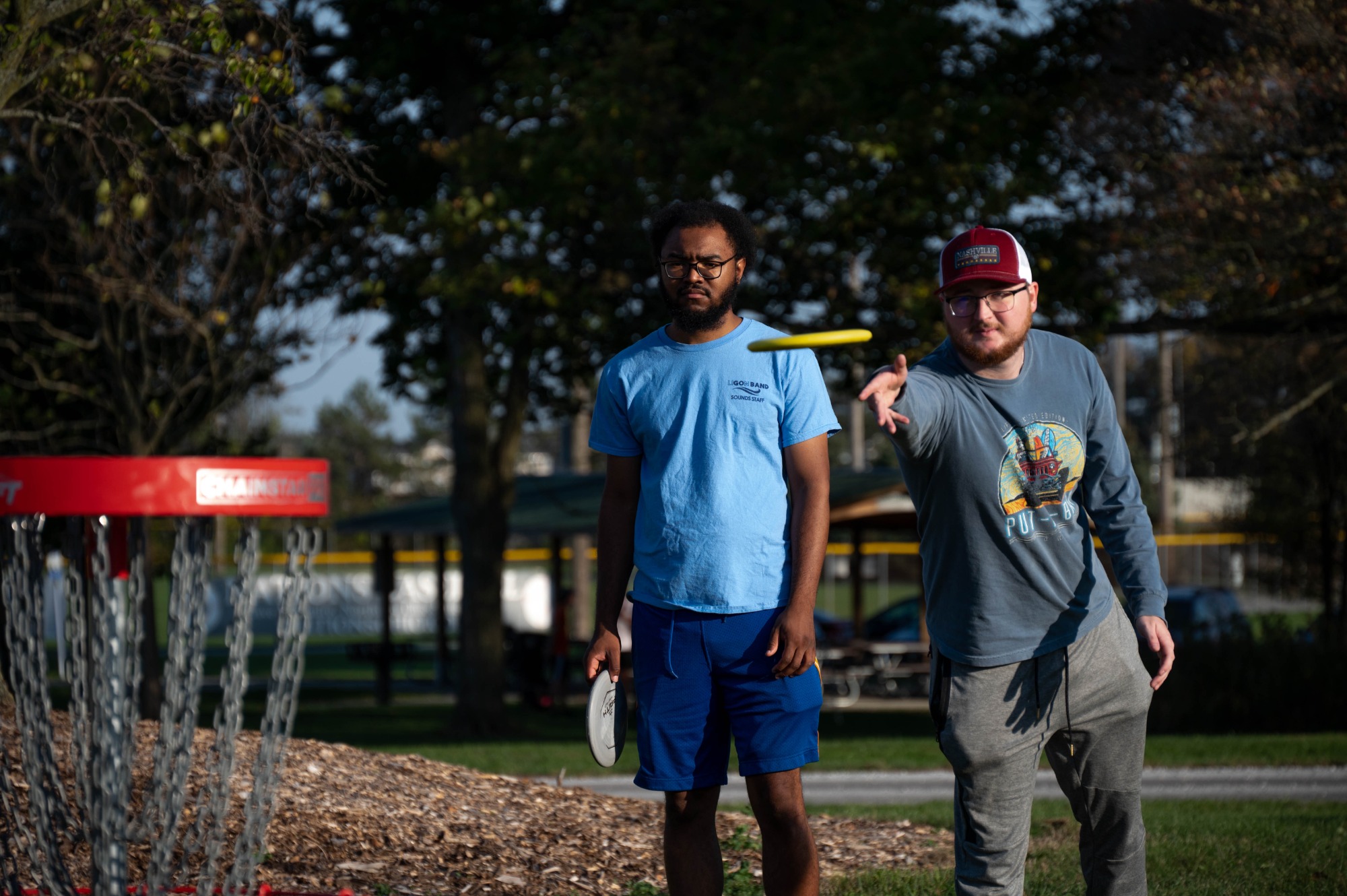 A member of the Club Disk Golf team releasing the disk, as he and his friend watch it go towards the basket 