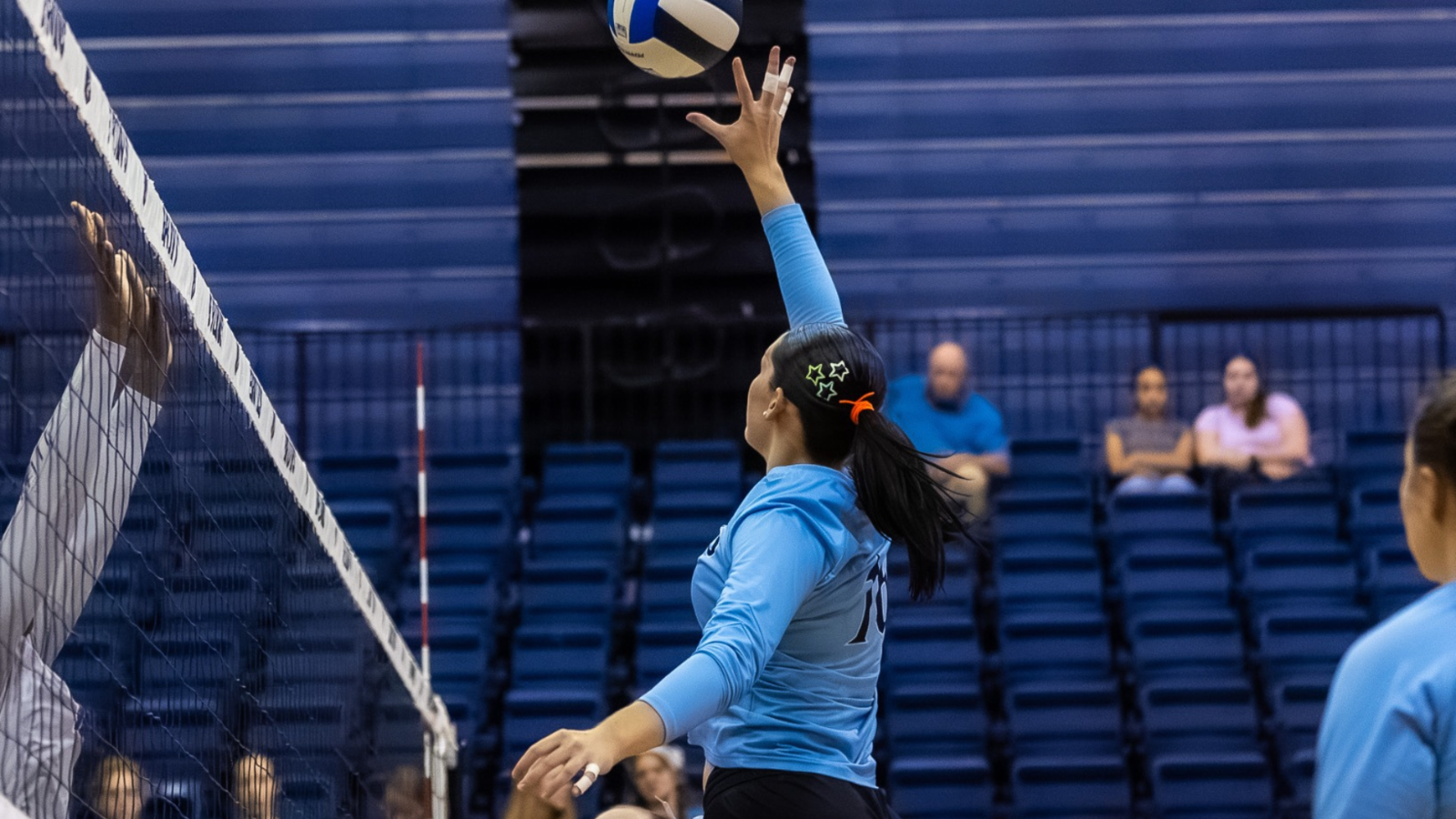 volleyball player in light blue jersey tipping the ball over the net