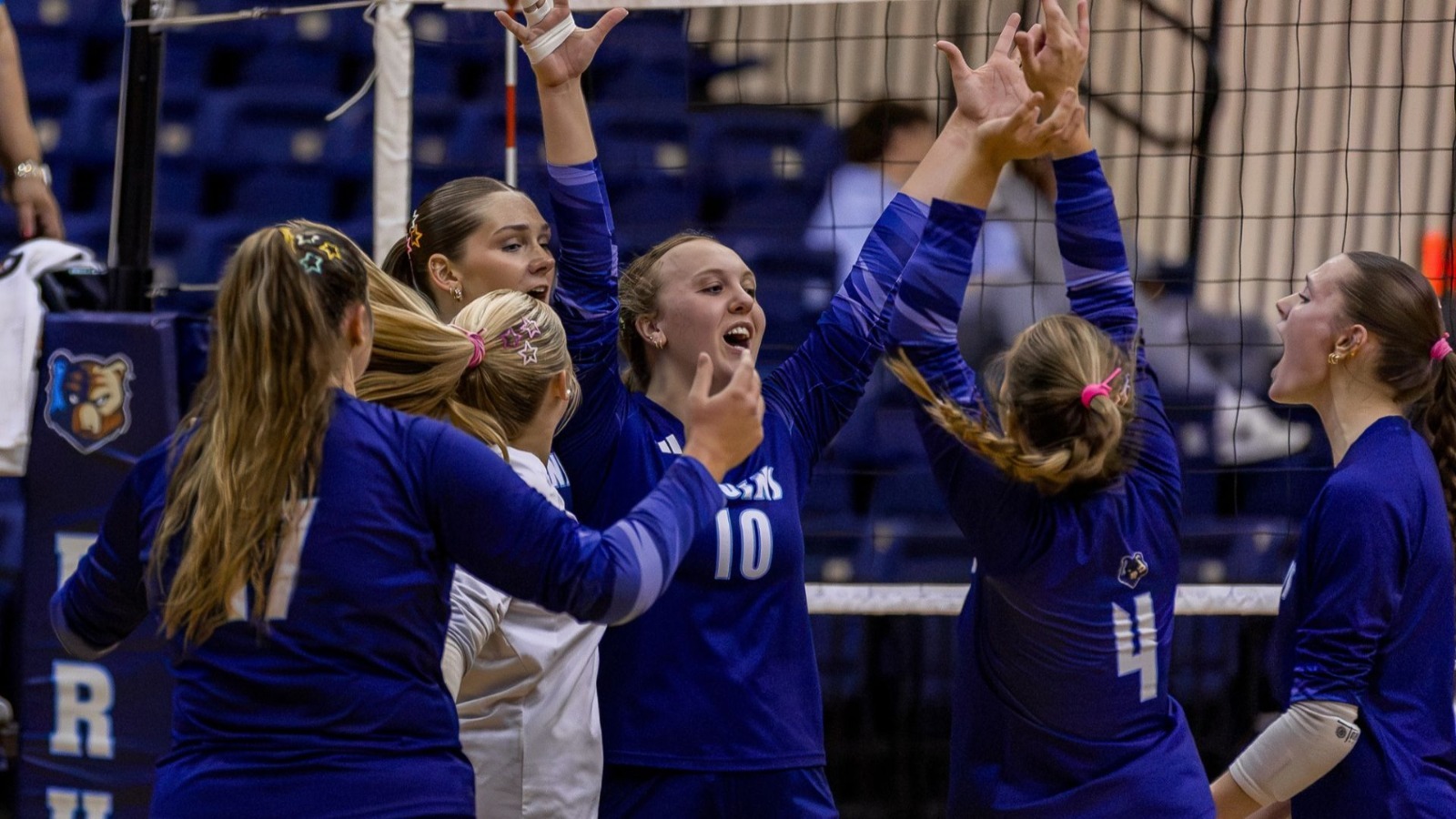 volleyball team in blue uniforms celebrating at the net