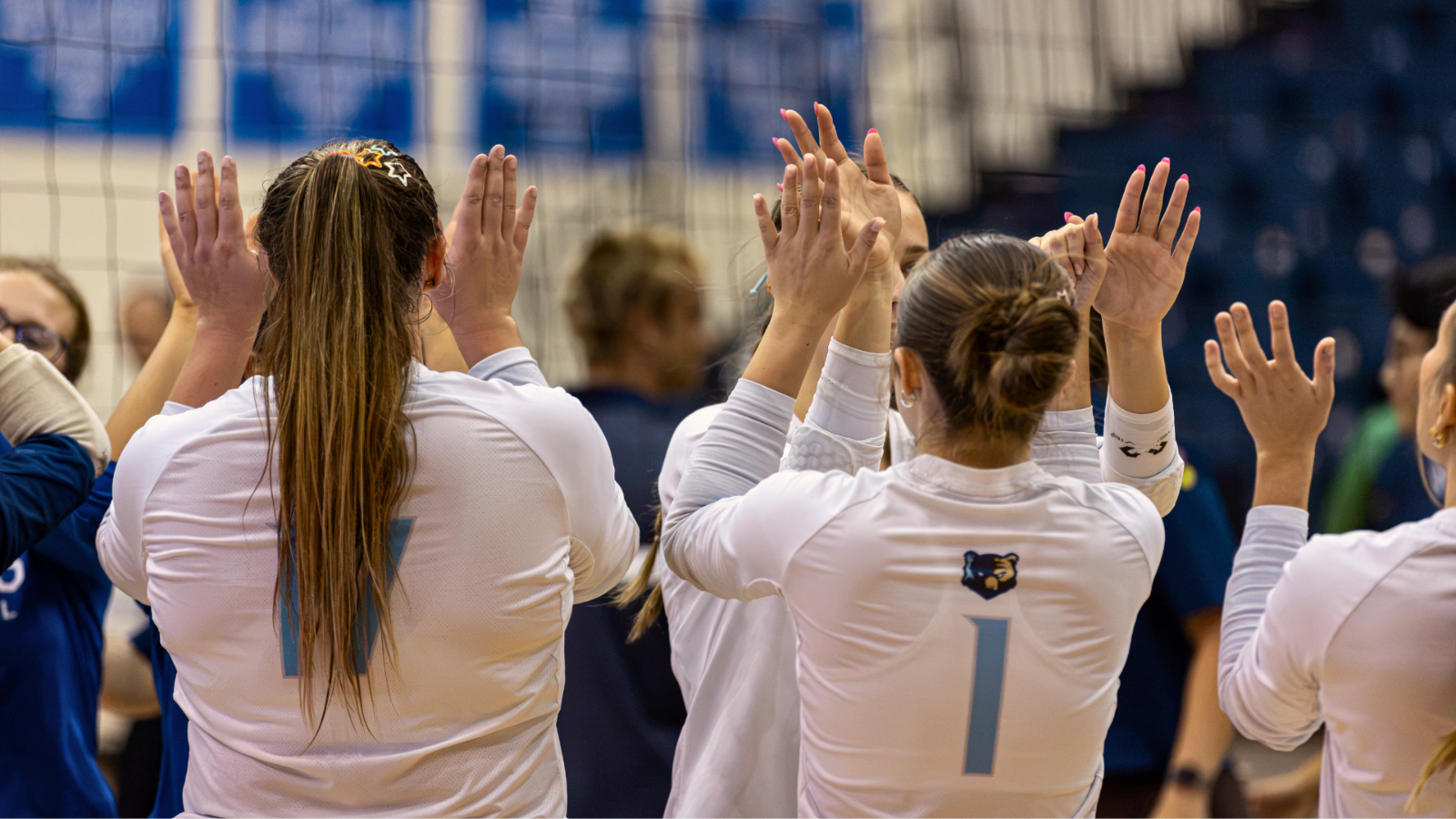 volleyball players wearing white jerseys giving their teammates a high five