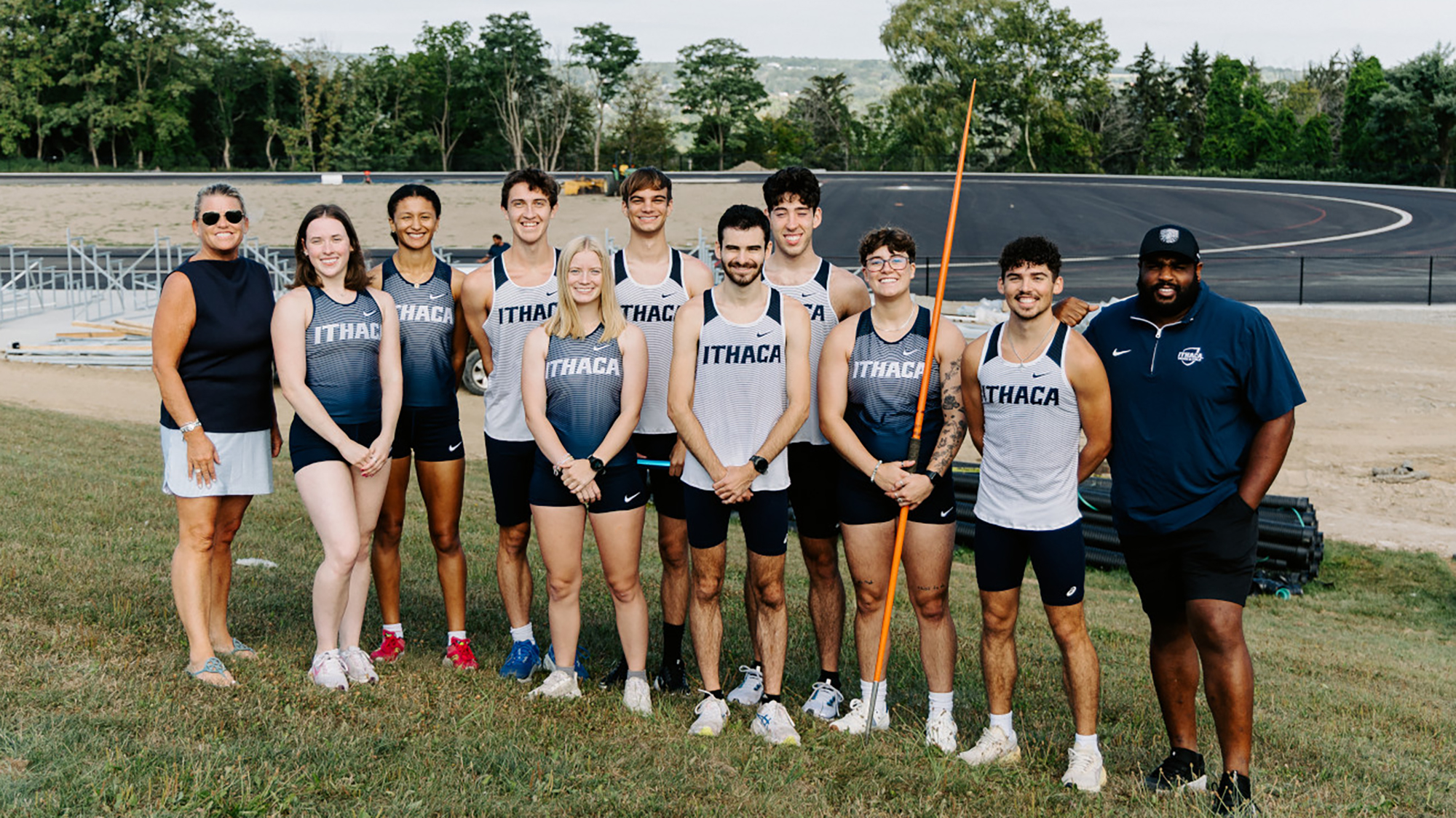 Athletes and coaches from the Men's and Women's track and field teams pose in front of the construction site of the new track in August 2025.