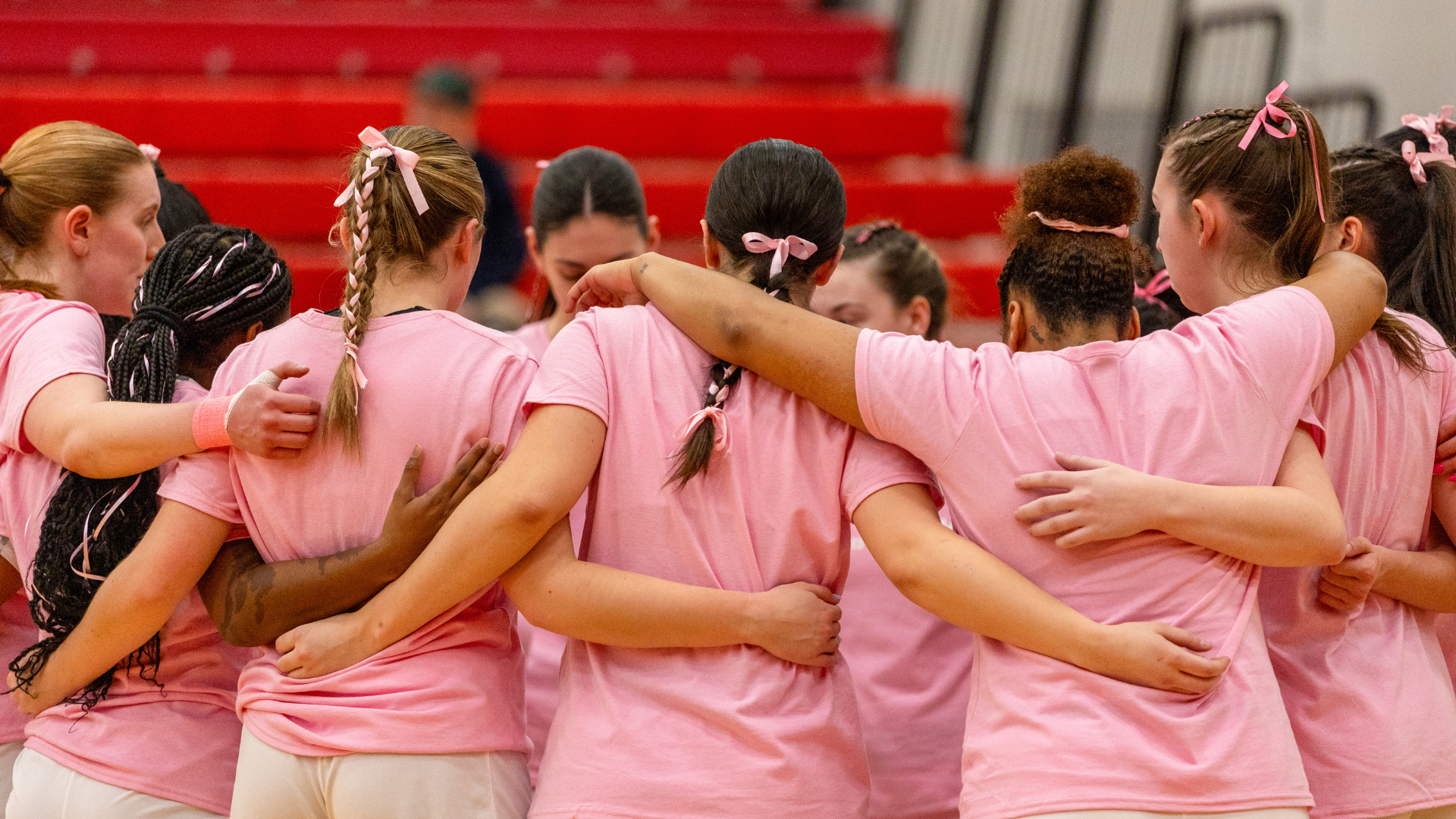 A group of Brock Badgers women’s basketball players wearing pink shirts huddle before the 2025 Shoot for the Cure Game.