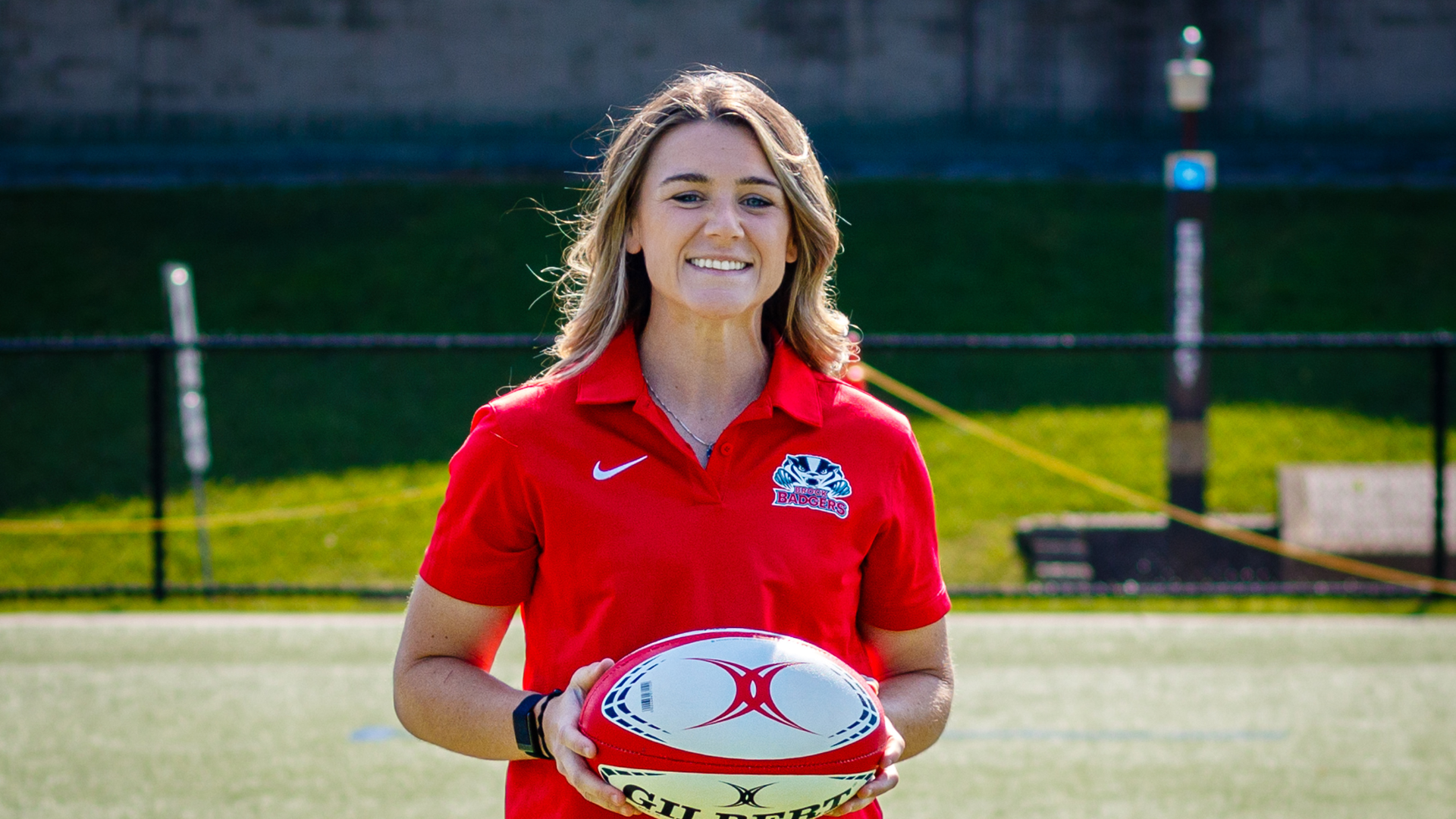 Lauryn Bons, the new women's rugby coach, pictured holding a rugby ball while wearing a Brock Badgers polo.