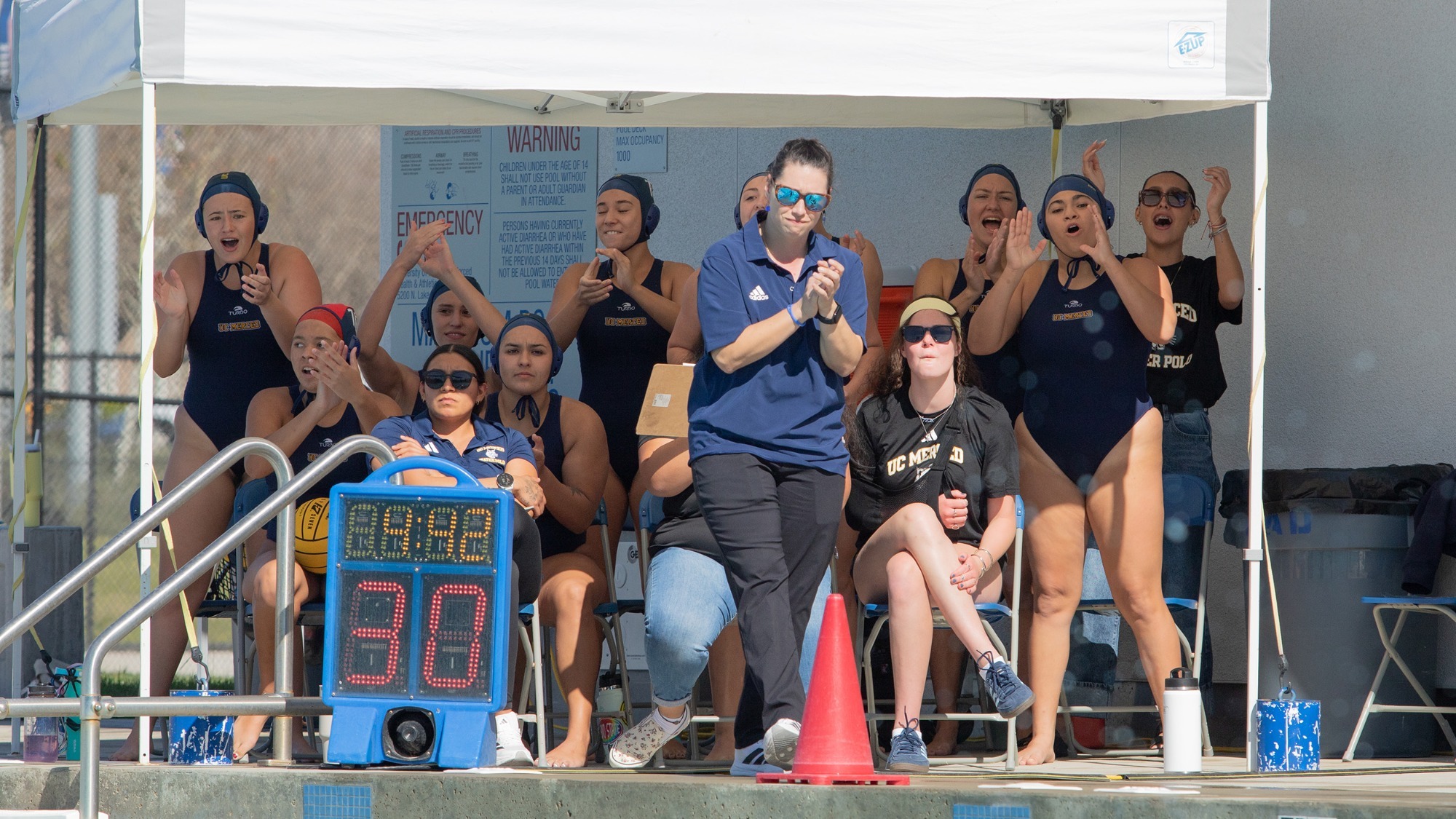 Women's water polo student-athletes and coaches cheering on the Bobcats from the pool deck.