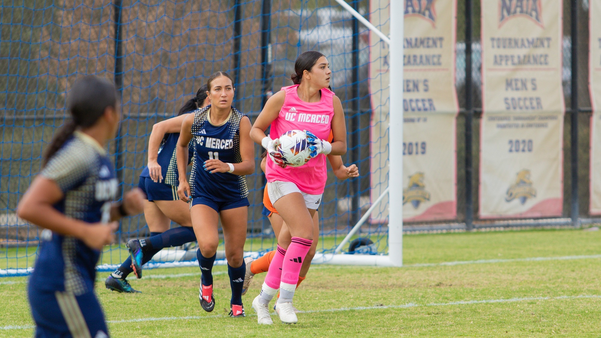 Goalkeeper Alicia Lepe in a pink jersey making a defensive play with her defenders on Bobcat Field.