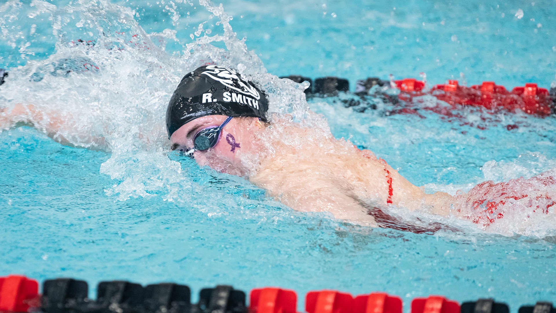 Swimmer Rachel Smith wearing a black cap with her name on it as she turns her head to breathe while swimming freestyle in a pool.