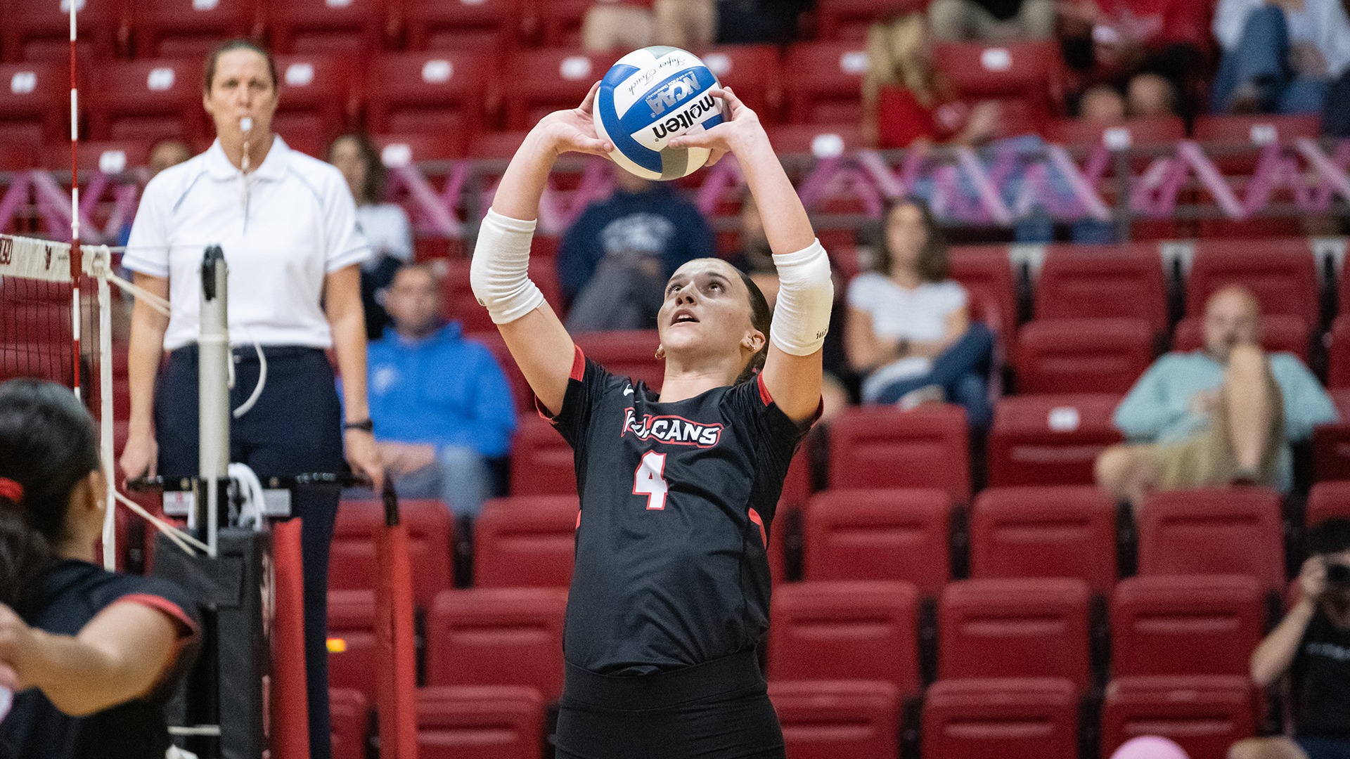California volleyball player Gracen Hartman (number 4) tracking the ball overhead with both hands raised, preparing to set during an indoor match.