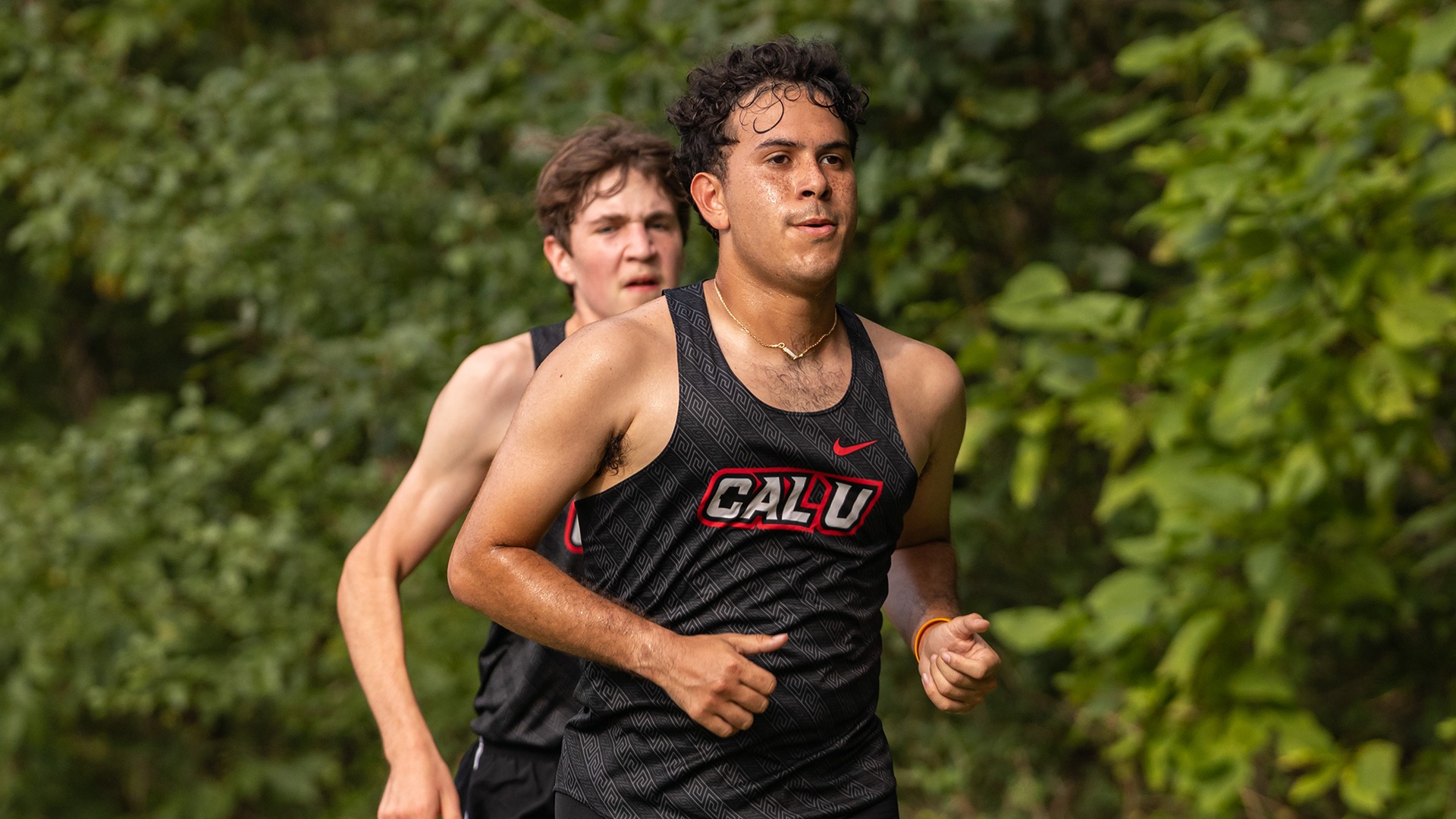 Amin Contreras runs along a shaded cross country course in a black Cal U tank top during a meet.