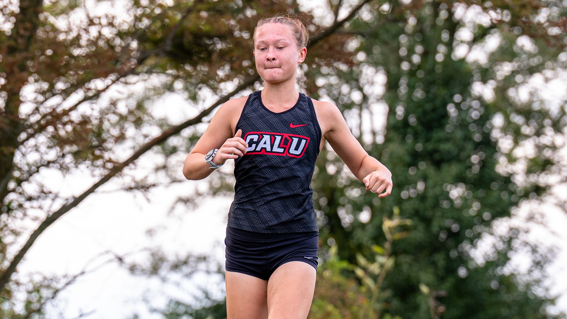 Sarah Sipe runs along an outdoor course wearing a Cal U uniform during a women's cross country meet.