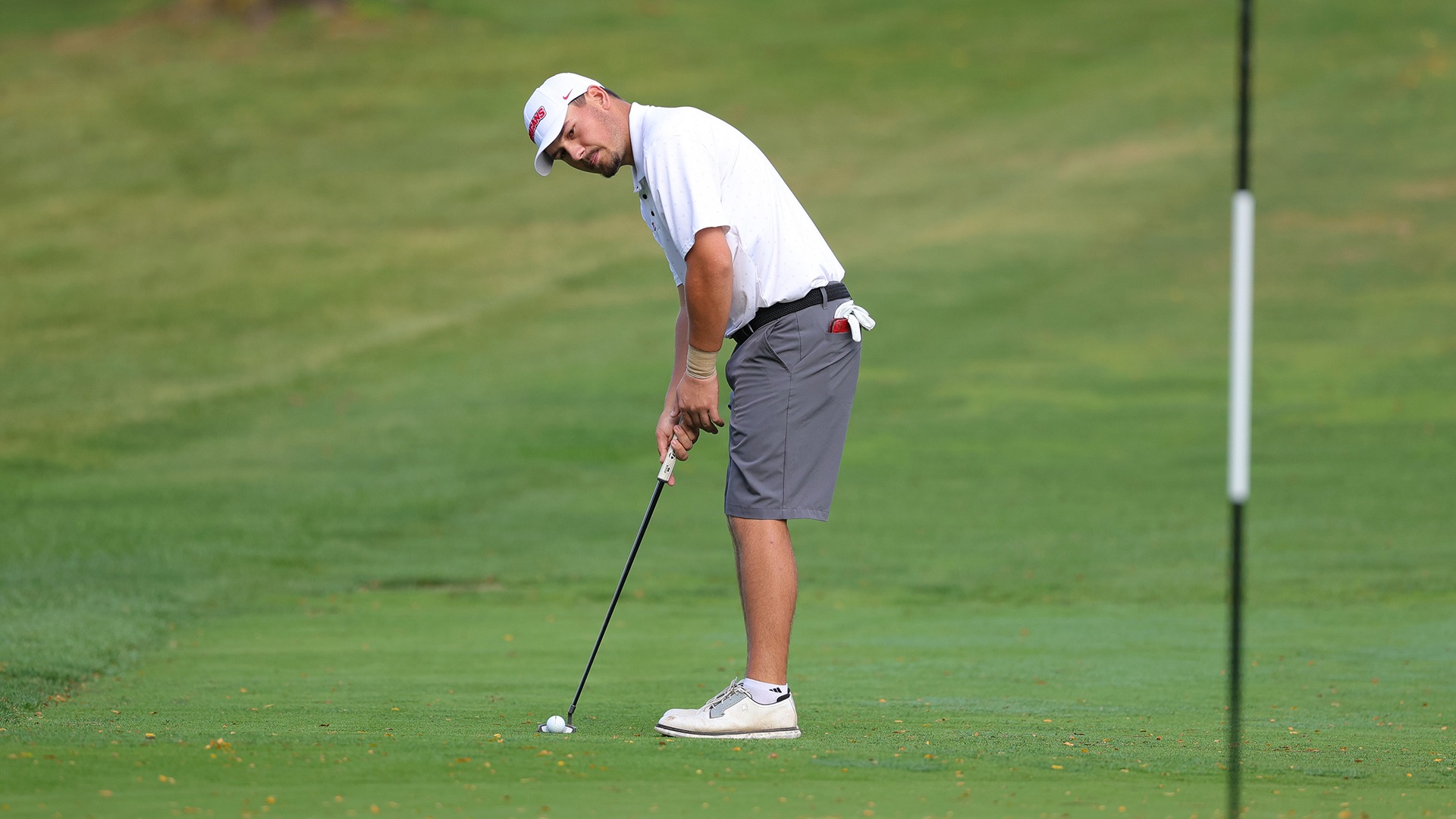 Nixen Erdely leans over a putt on the green near the flagstick during a California men's golf tournament.