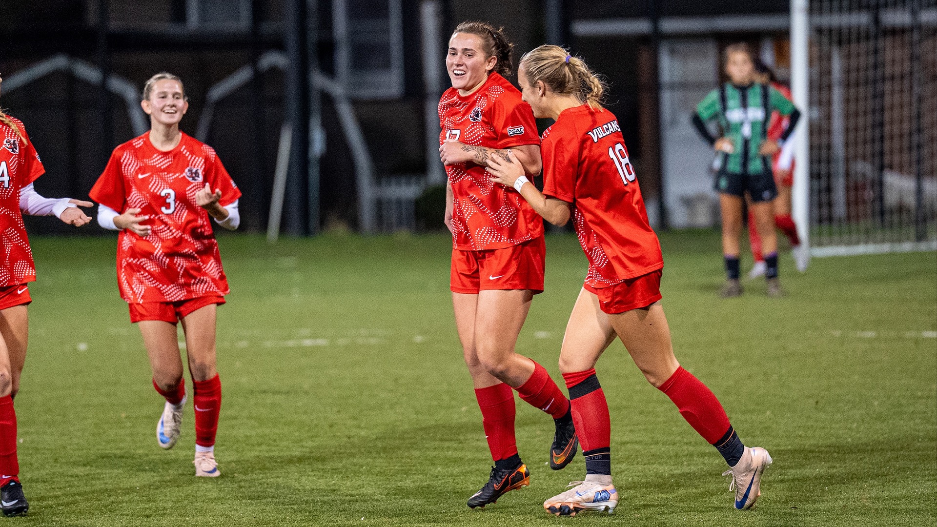 California women's soccer player Macrina Robb smiles while celebrating a goal on the field with a teammate wearing jersey number 18.