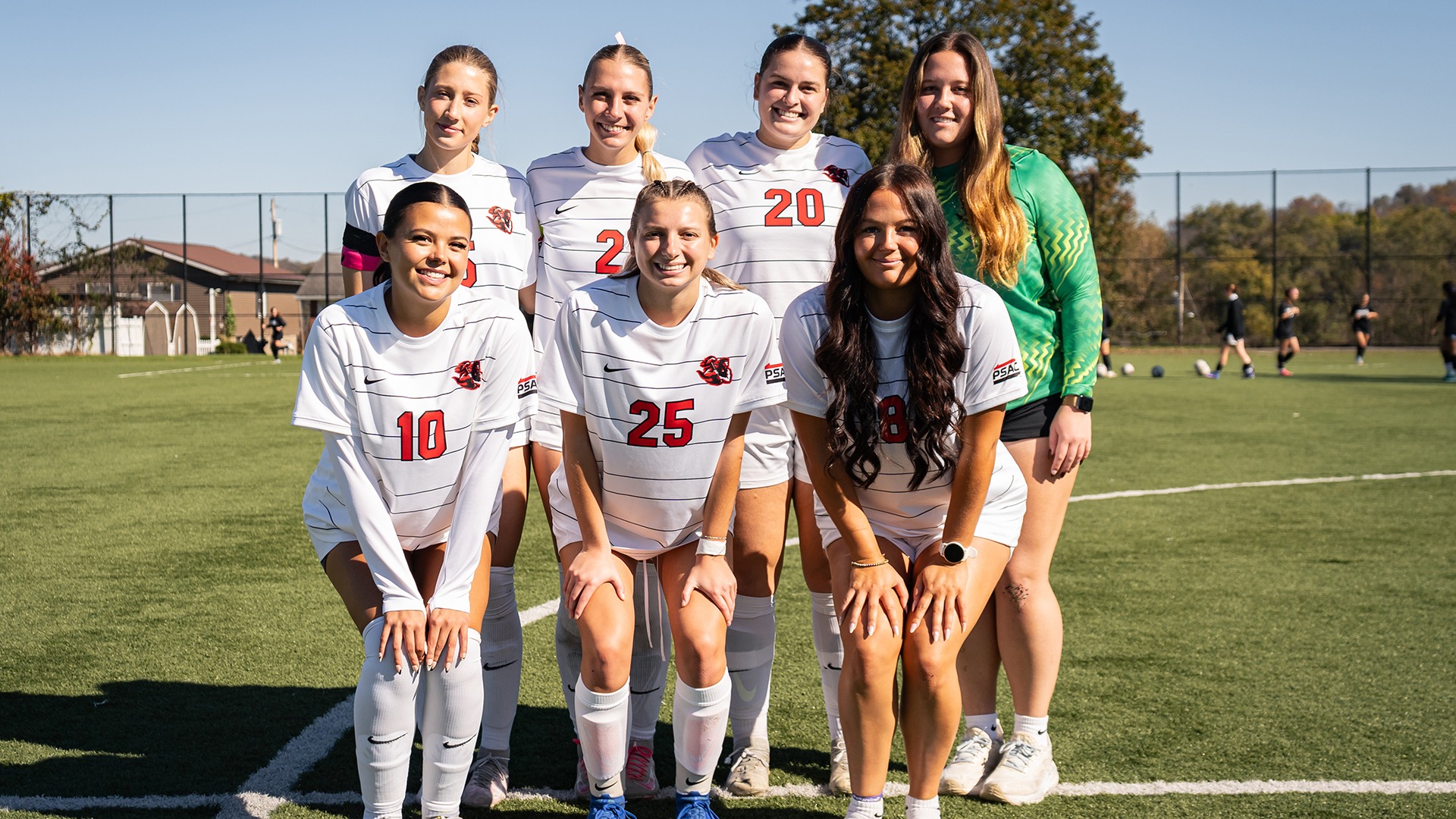 Seven members of the California women's soccer team pose together on the field in uniform.