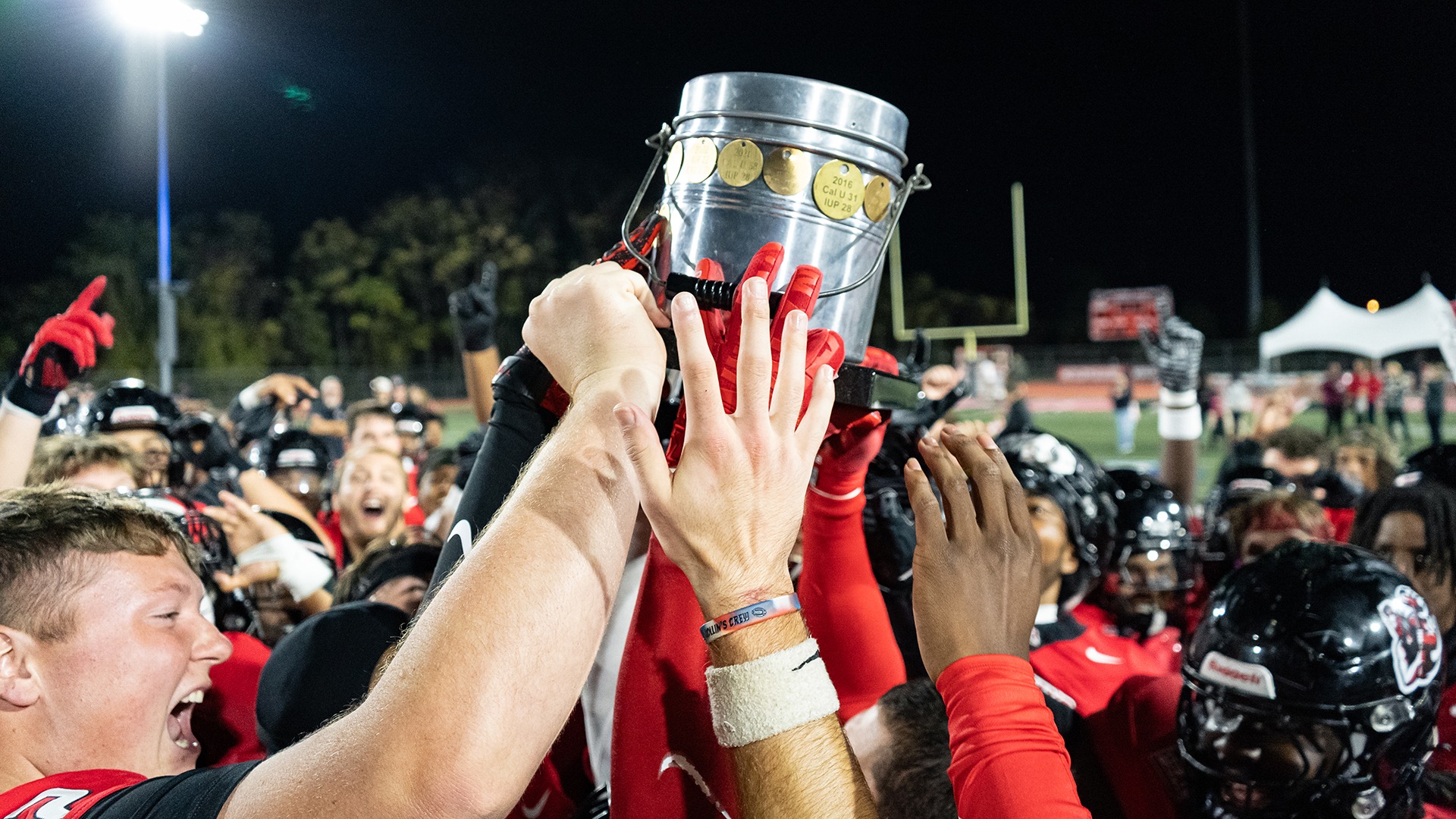 California football players hoist the Coal Bowl trophy together in celebration on the field after defeating IUP