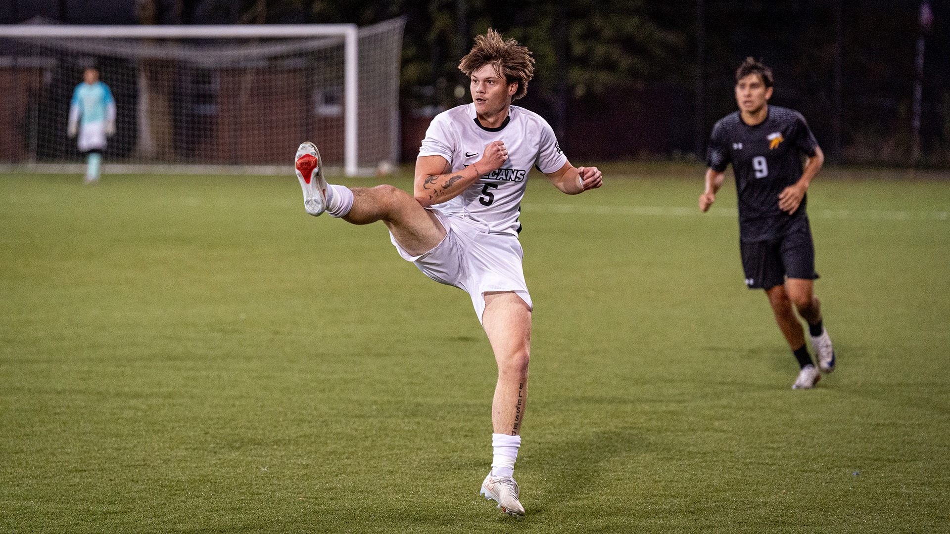 Thomas Ruffcorn (No. 5) extends his leg high to clear or control a ball during a men's soccer match