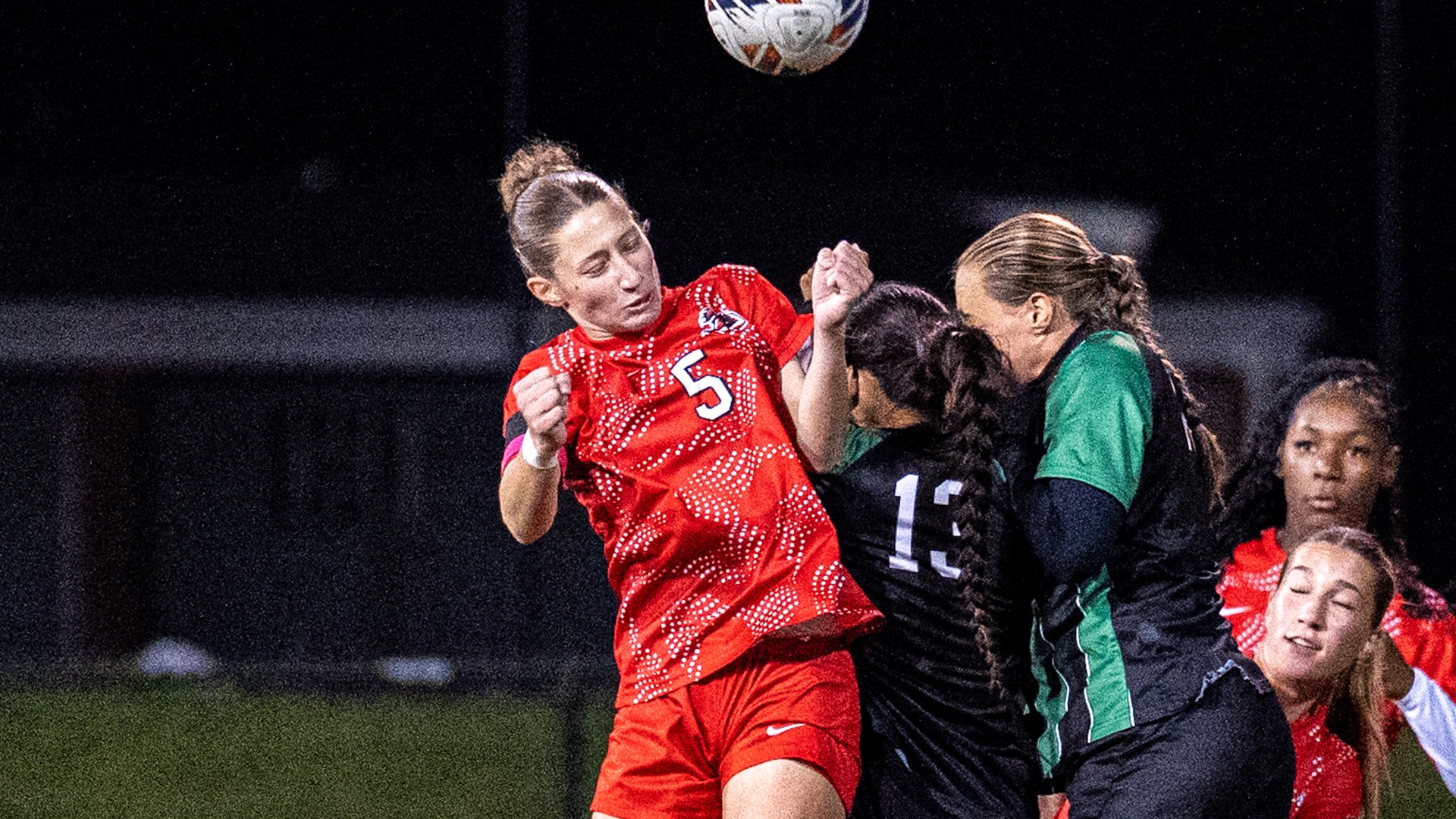 Caelin Thomas (No. 5) leaps to head a soccer ball in traffic during a night match.