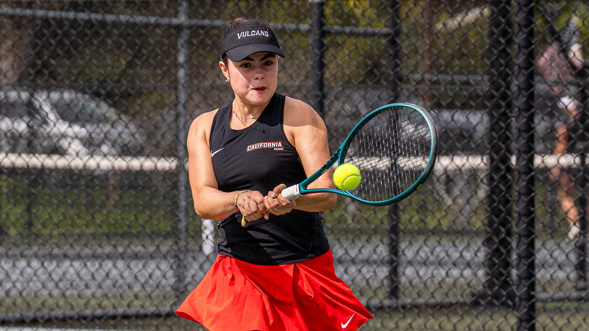 California tennis player Fernanda Sandoval Martinez tracking a yellow tennis ball mid-air as she prepares to hit a two-handed backhand on an outdoor court.