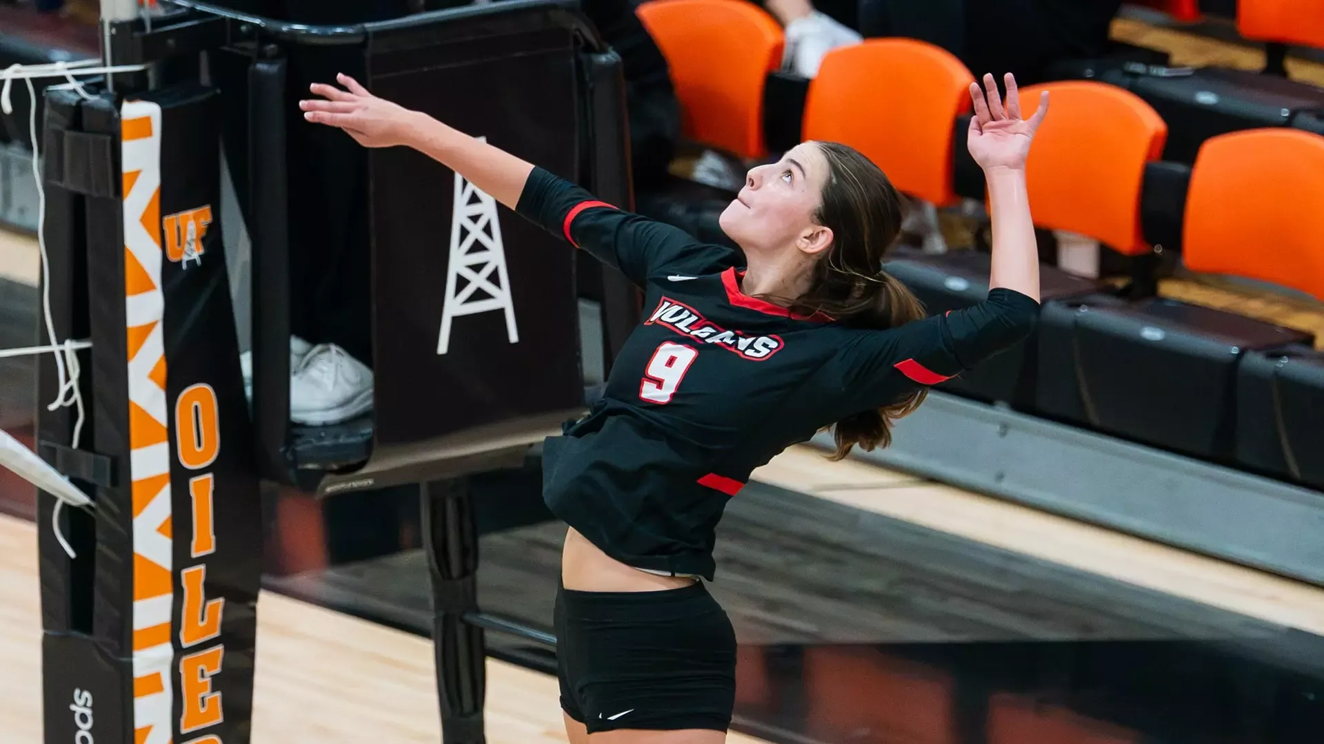 Madelyn Salisbury (#9) in a black jersey leaps mid-air near the net to strike the ball during a match against the Findlay Oilers.