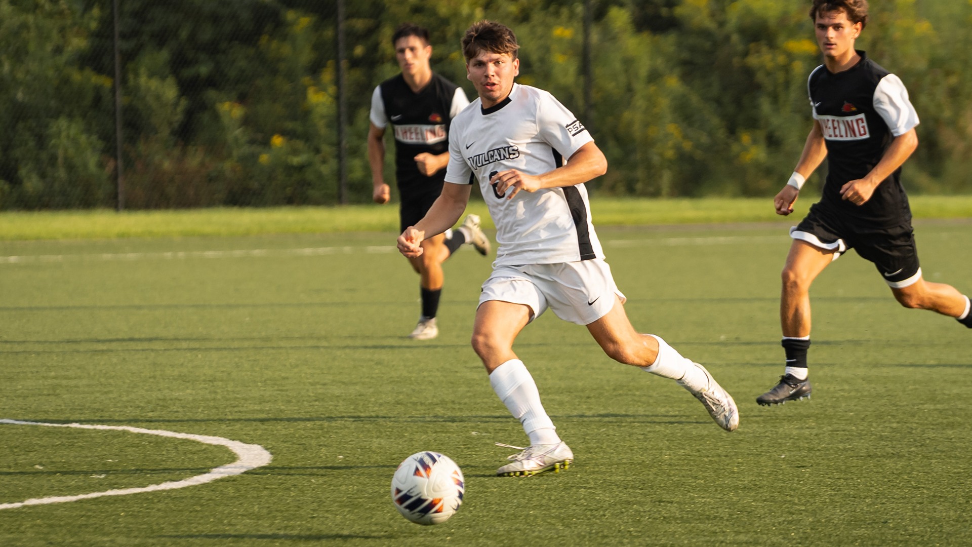 California men's soccer player Seth Basinger (#6) dribbles the soccer ball downfield past opposing Wheeling University defenders during a match.
