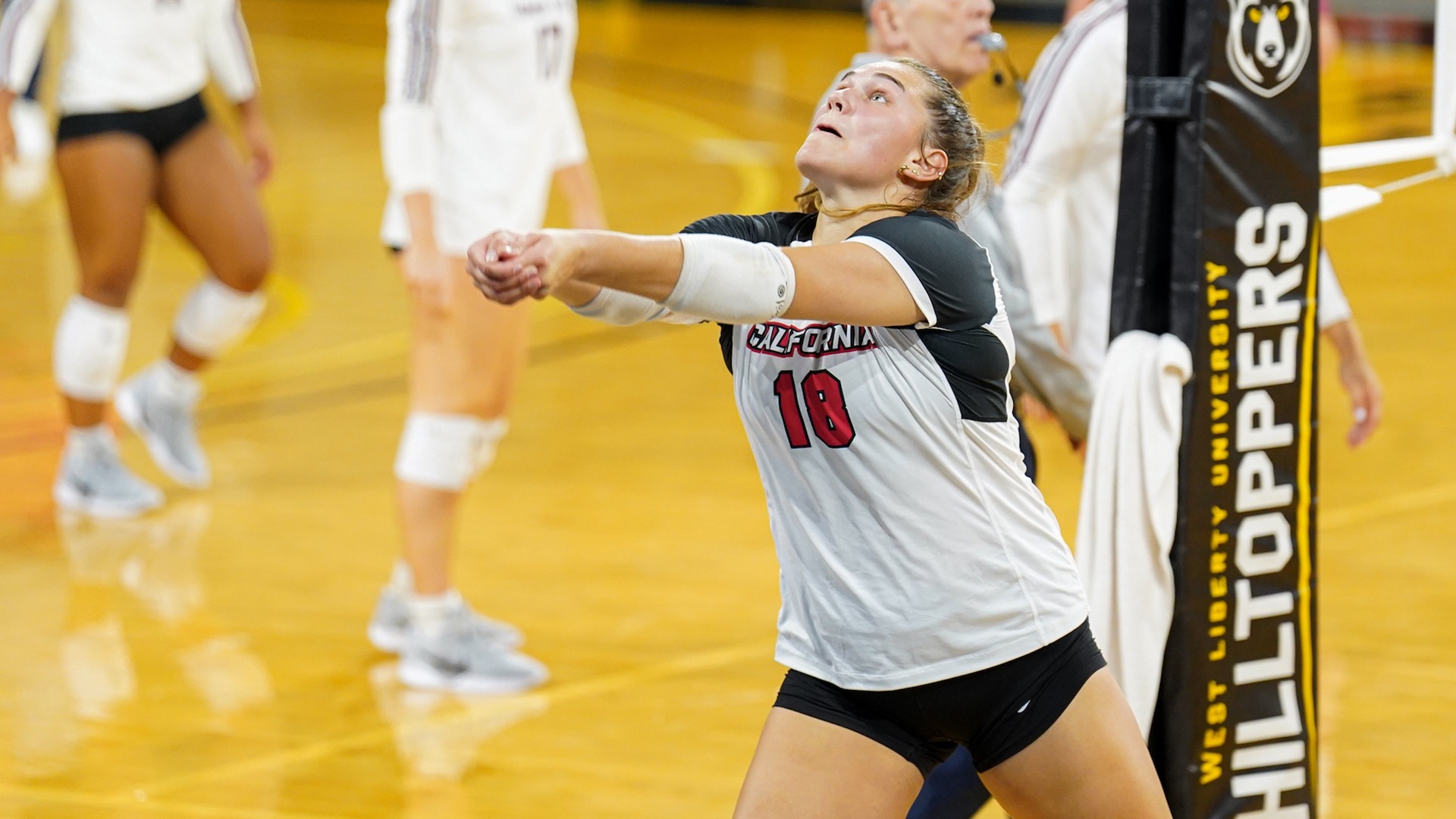 Volleyball player Tori Newton (#18) in a white jersey bumping a ball during a indoor match near the net.