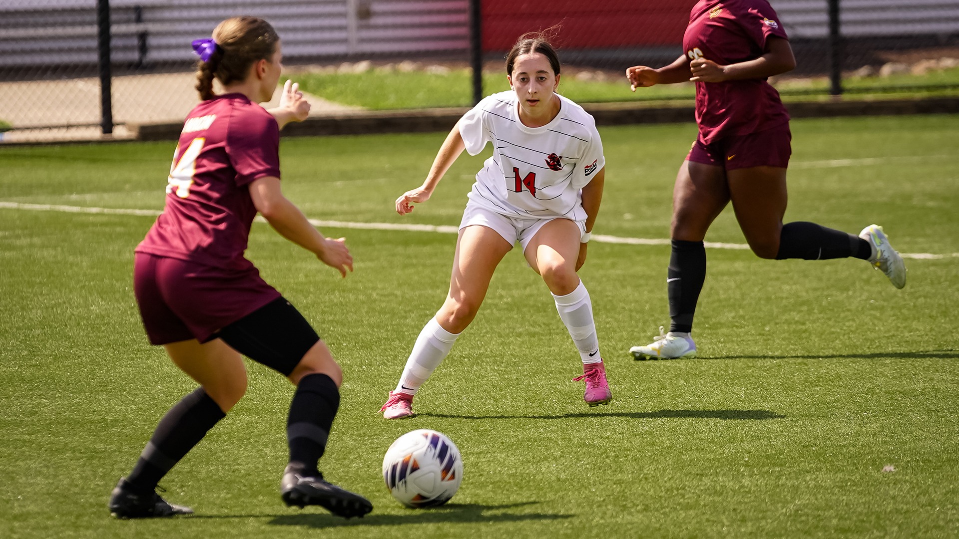 Julia Flynn (#14) controls the ball while being defended by two Gannon players during a soccer game.