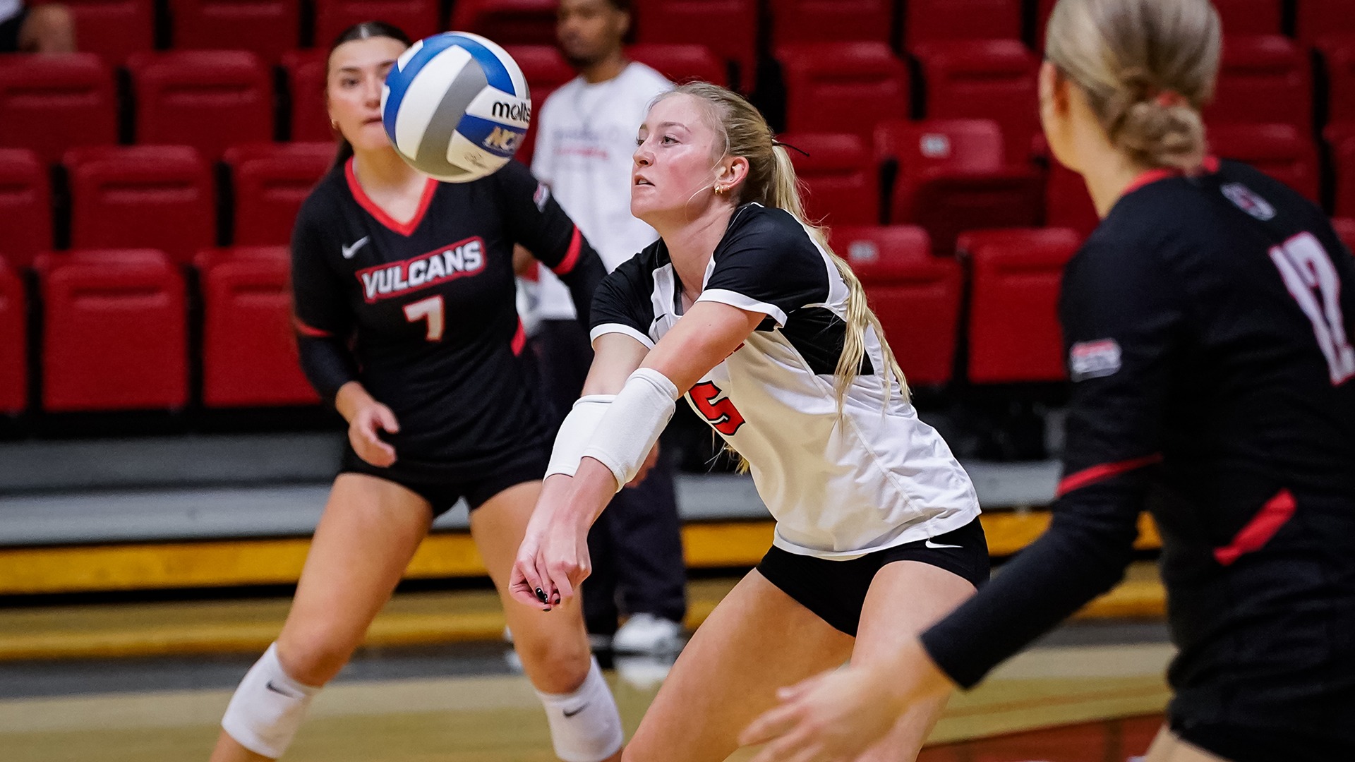 Alece Evanto bumps a volleyball in a white jersey during a match against Pitt-Johnstown, with teammates in black jerseys nearby.