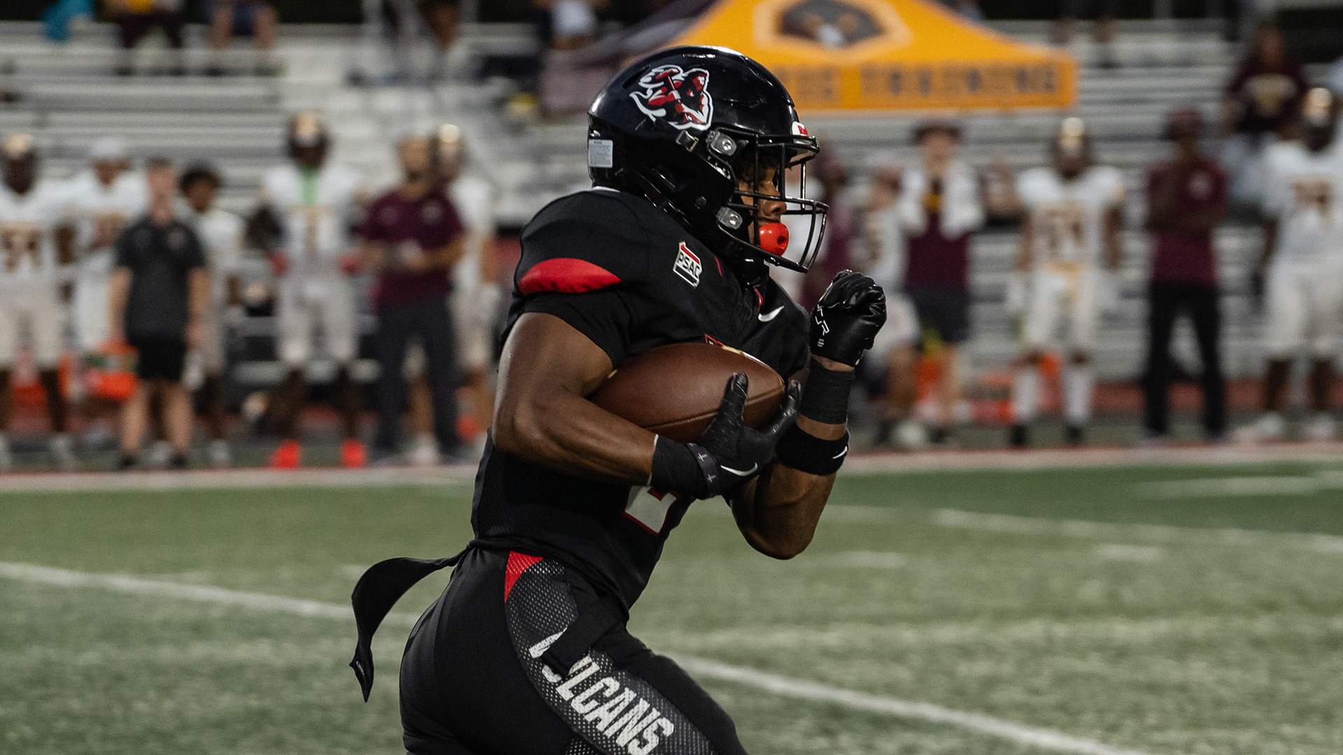 Bobbie Boyd Jr. carries a football down the field in black uniform during a game, holding the ball securely with black gloved hands.