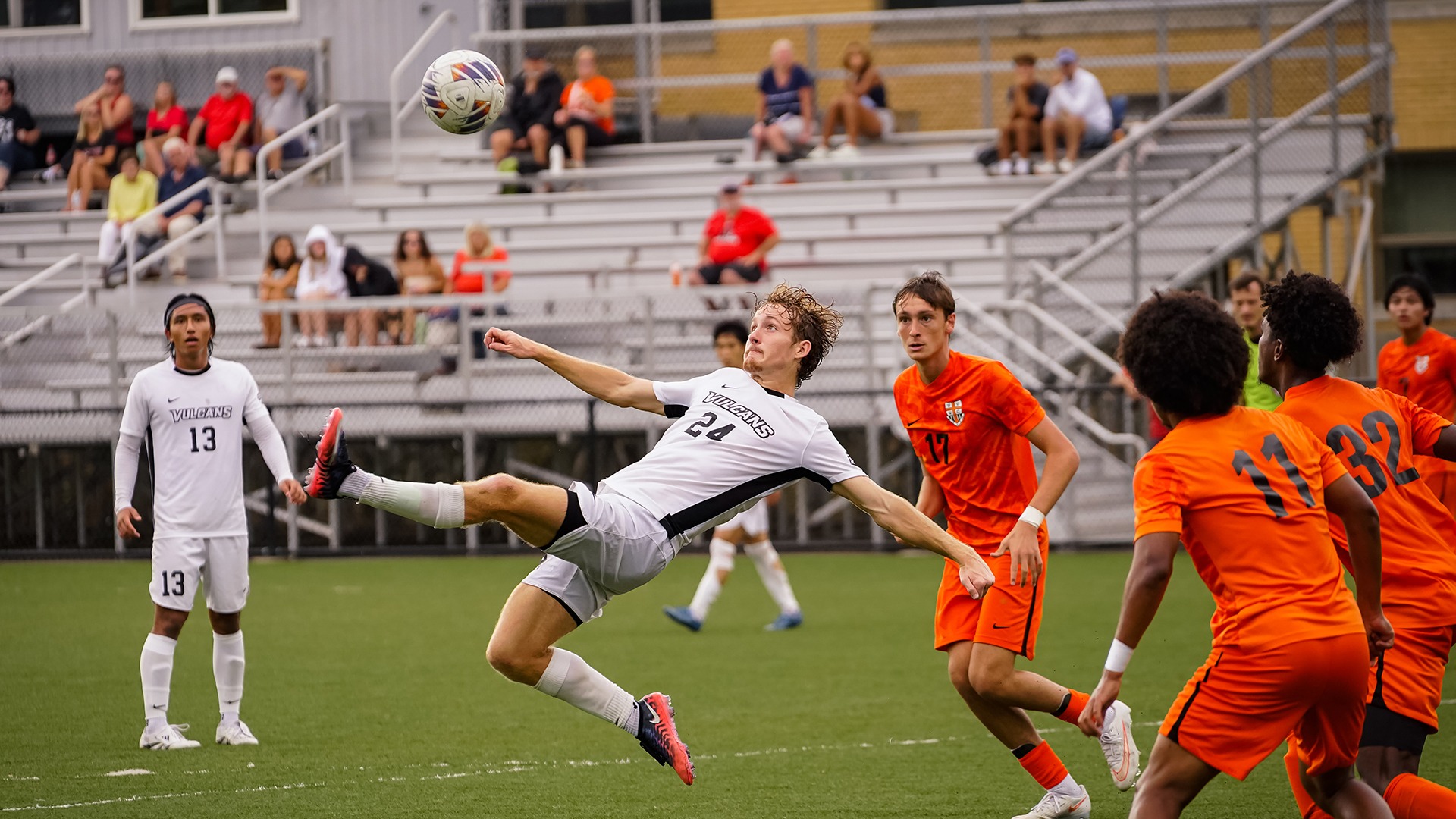Cole Radcliffe jumps horizontally mid-air to kick a soccer ball against West Virginia Wesleyan during a match on the field.