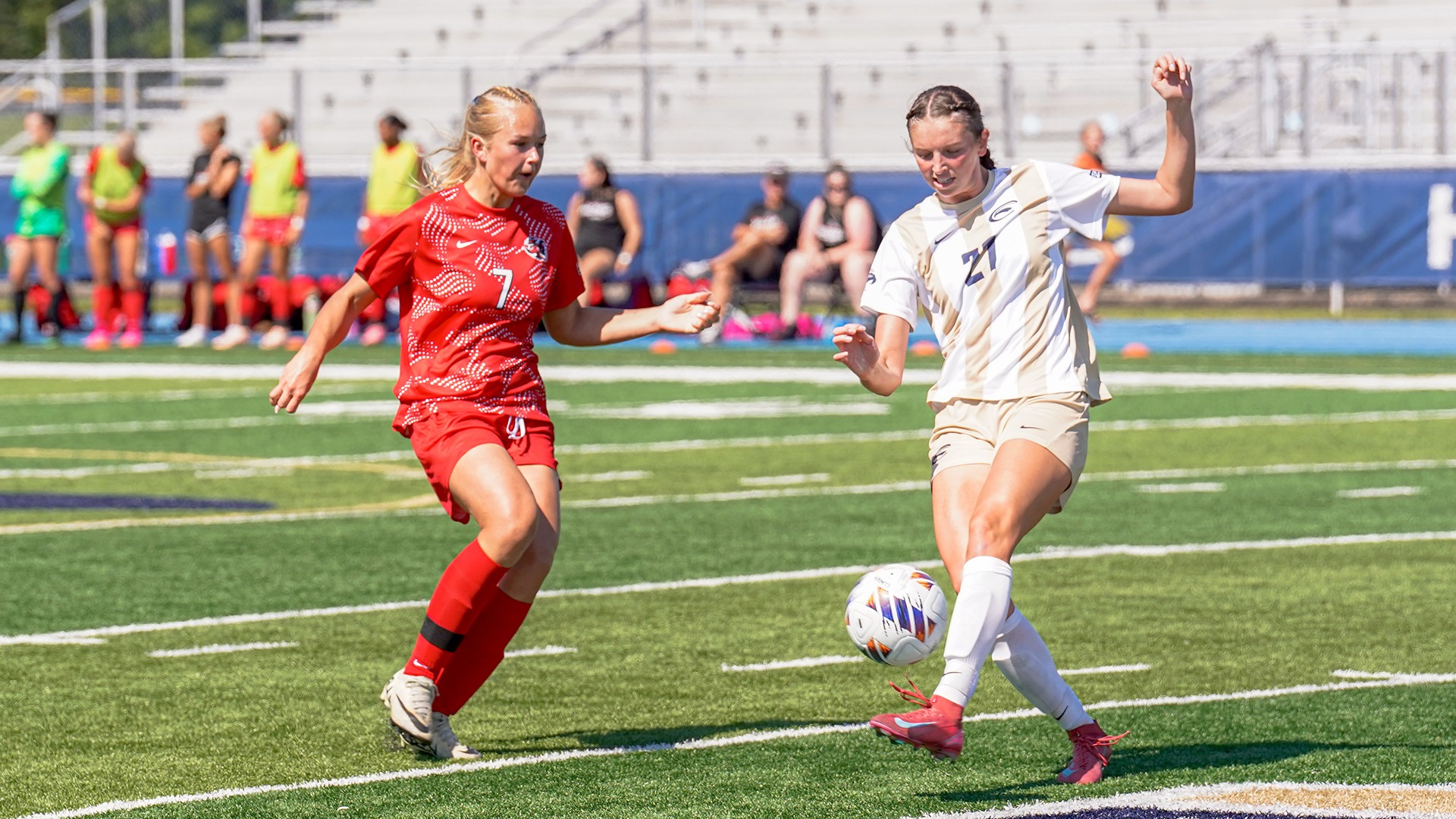 Hedda Bjoerkman in red defends against a Clarion soccer player in white controlling the ball during a match on the field.