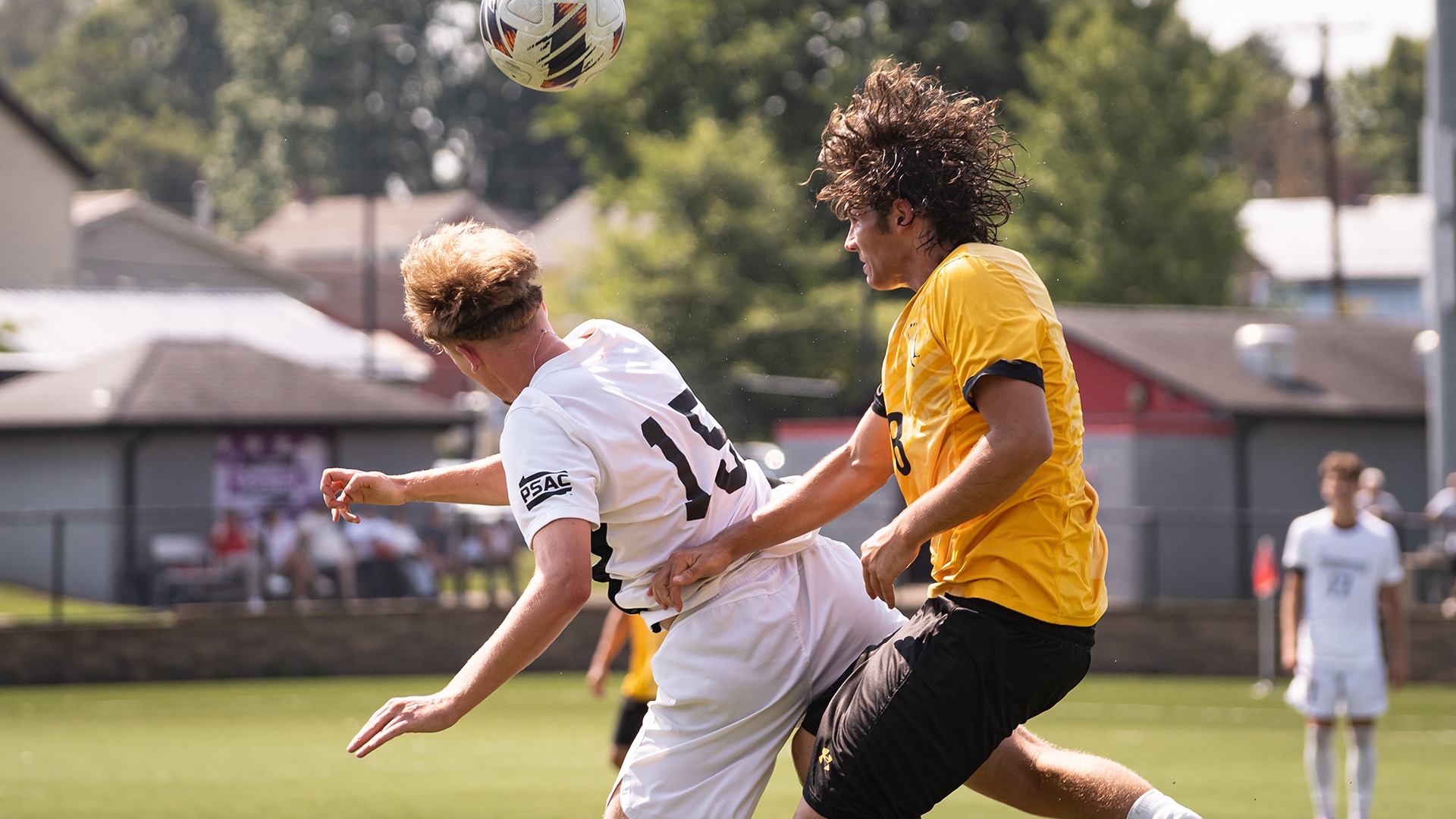 California soccer player Jan Sebest wearing a white jersey with the number 19 leaps backward to attempt a header while competing against a player from Millersville in a yellow jersey.