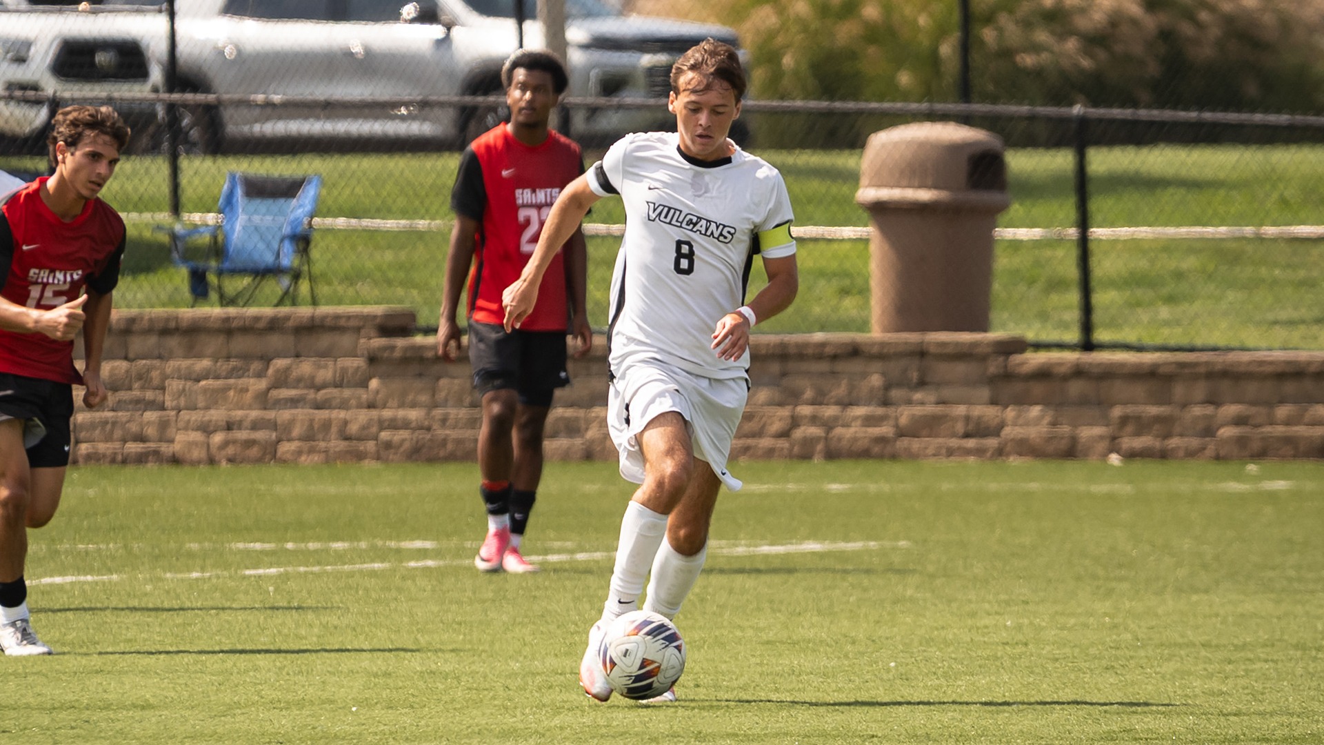 Soccer player Jacob Gretz (#8) dribbles a soccer ball down the field in a white uniform during a match while opponent players follow behind.