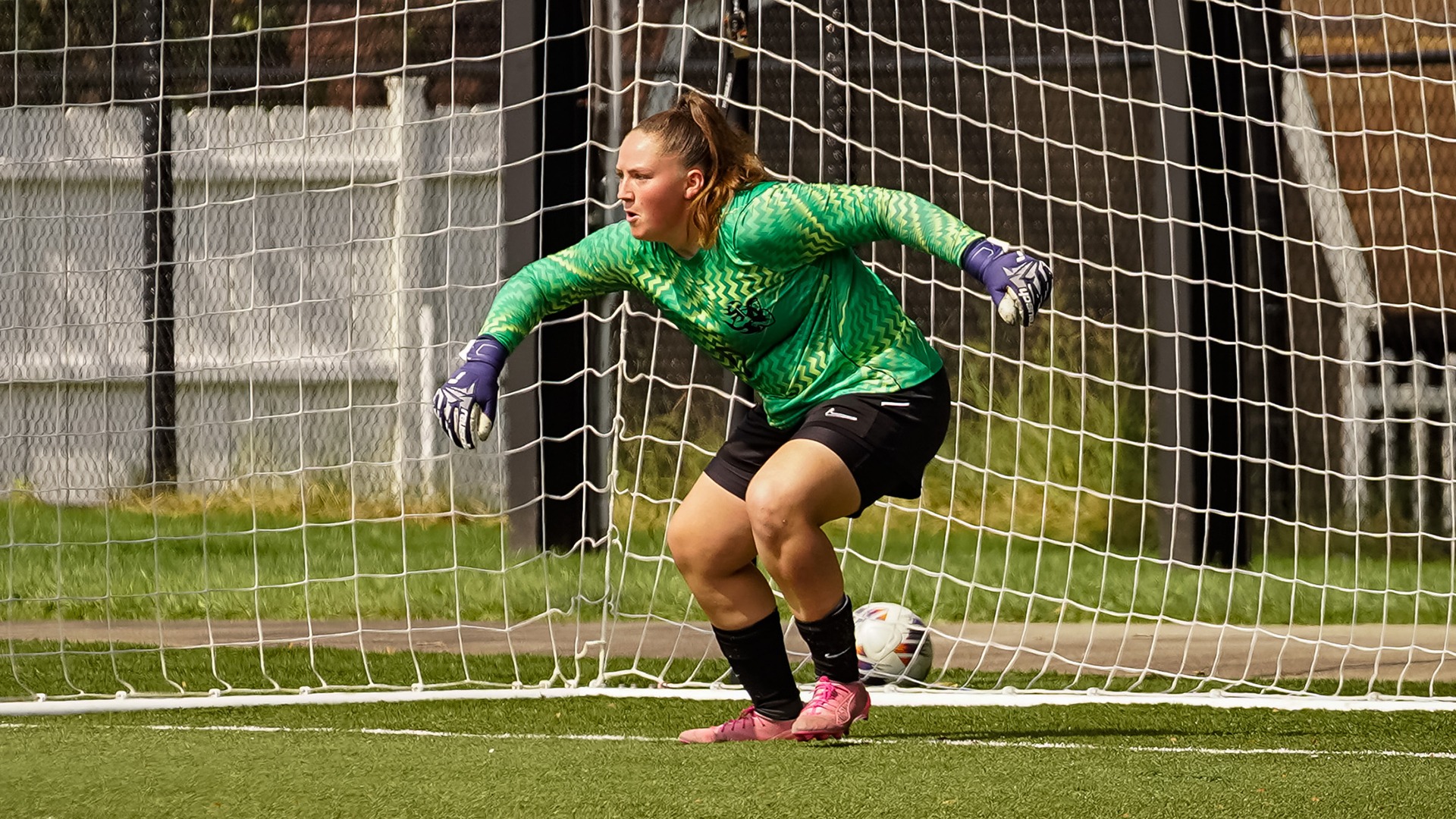 Soccer goalie Kaleigh Rexroad stands in a ready stance in front of the net in a green jersey and purple gloves during a game.